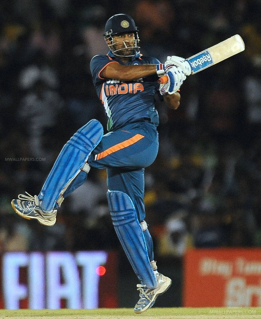 MS Dhoni 桌布 壁紙 — 一名身穿藍色球衣的印度板球運動員在夜間比賽中於球場燈光下跳起揮棒。