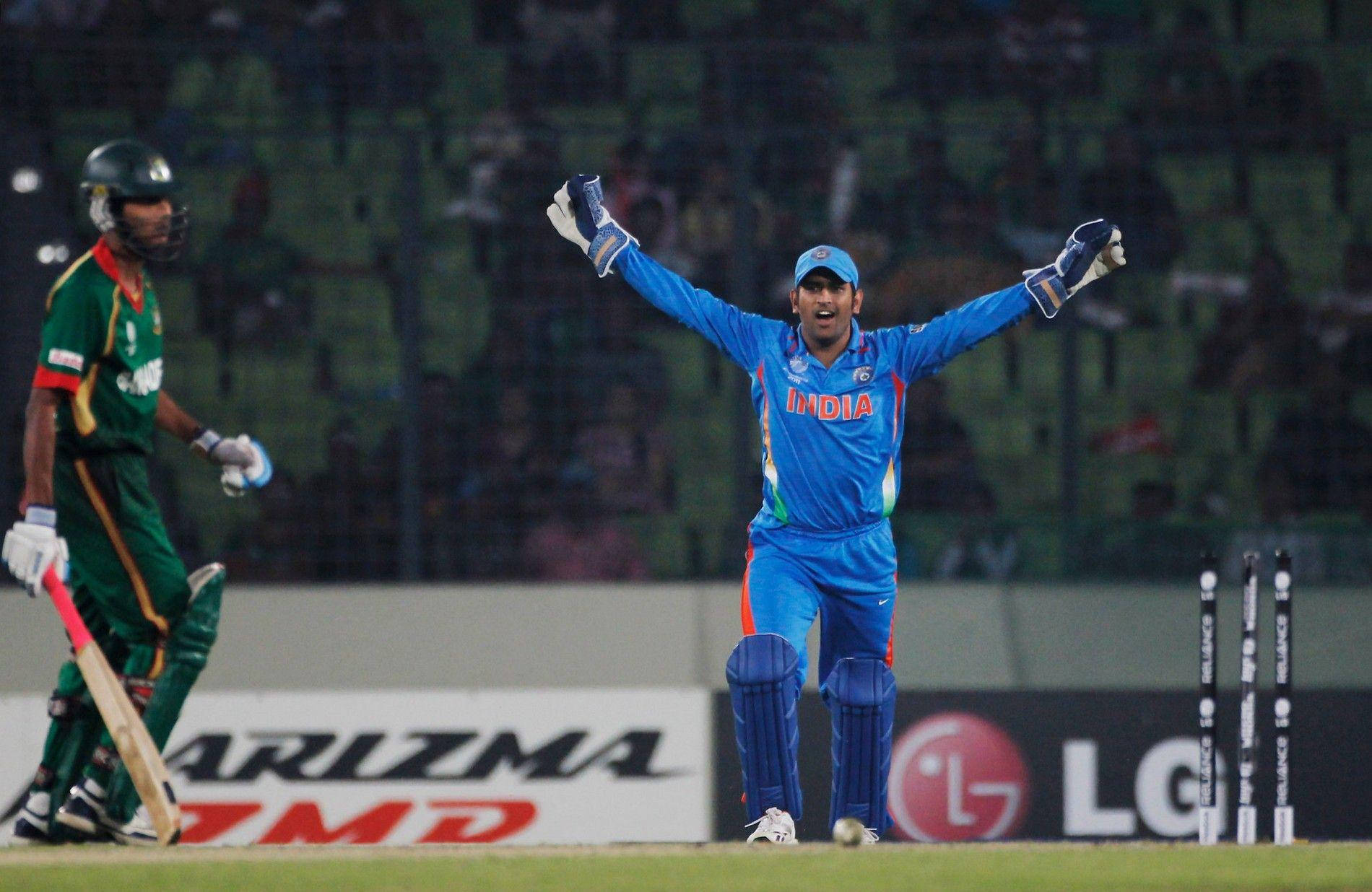 Ms Dhoni 桌布 壁紙 — 一名身穿藍色球衣的印度板球運動員在燈光球場上高舉雙臂慶祝勝利，而一名孟加拉擊球手正離場。