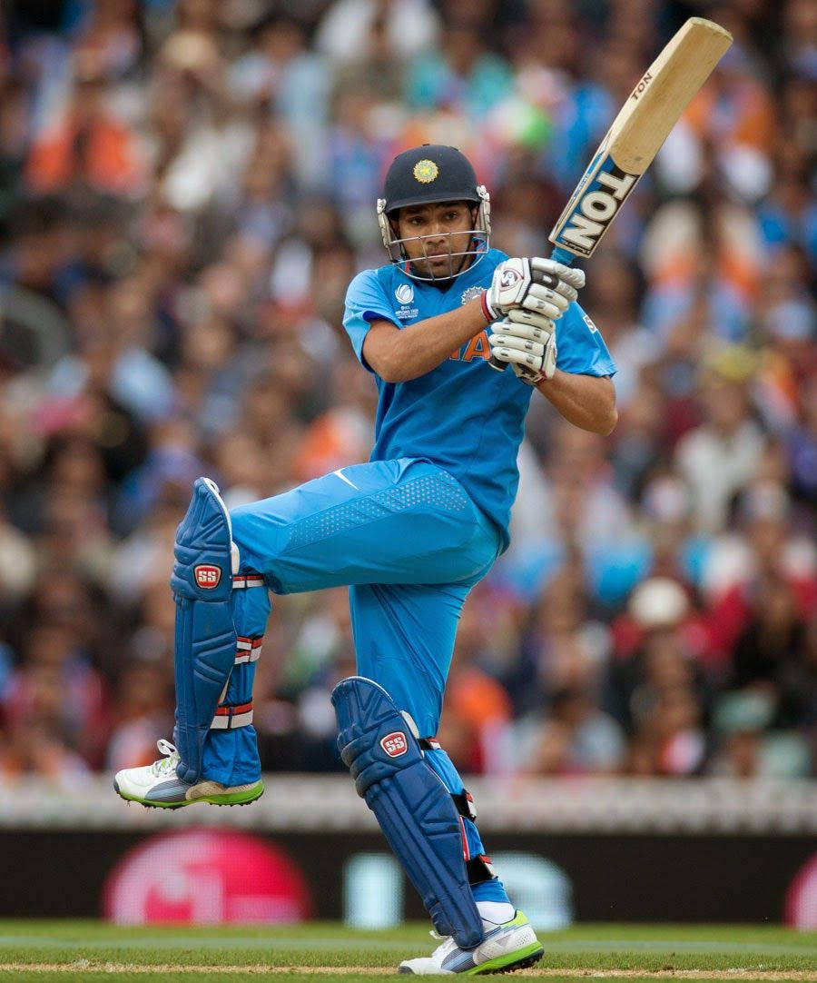Rohit Sharma 桌布 壁紙 — 一名身穿藍色球衣的板球擊球手，在模糊的體育場人群背景下高舉球棒揮擊。