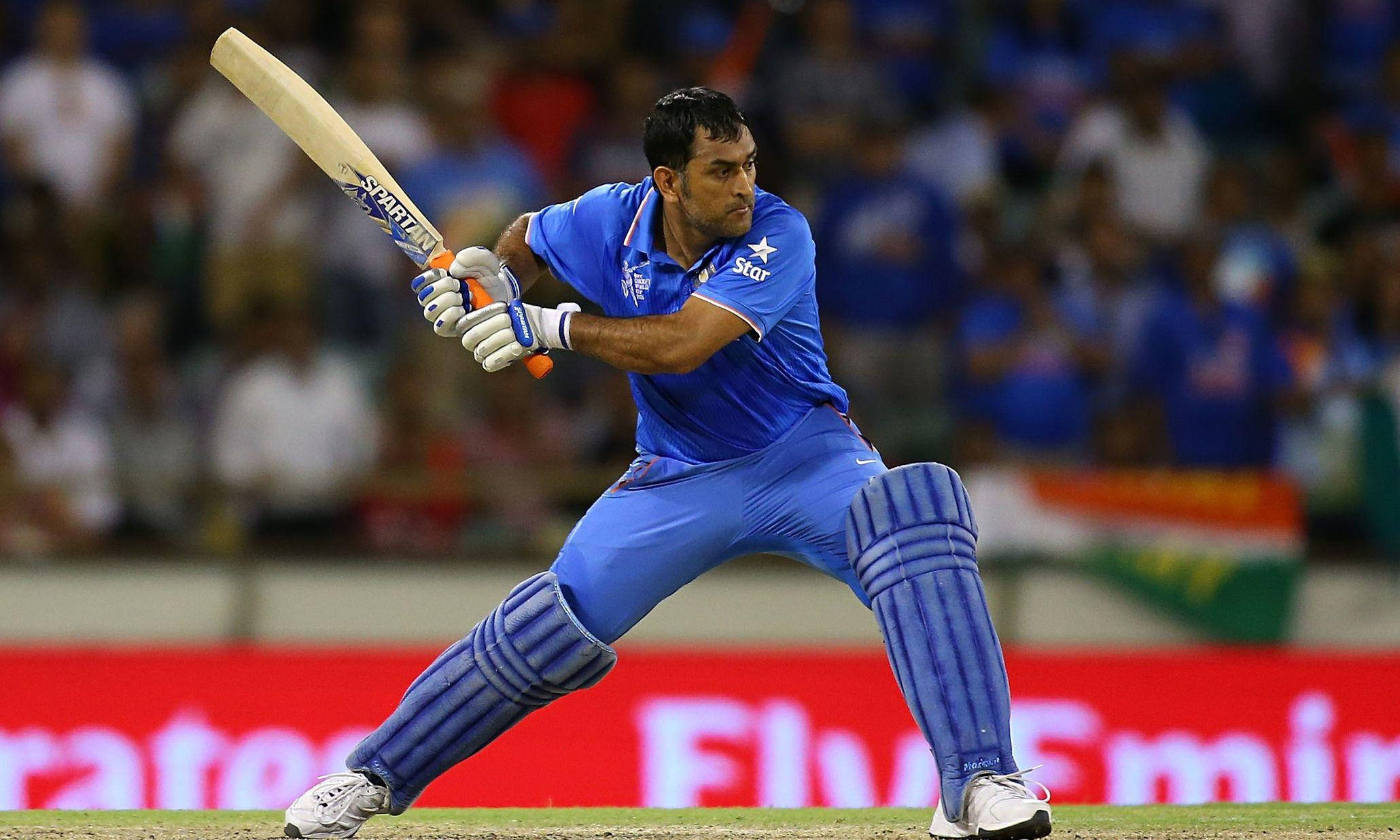Ms Dhoni 桌布 壁紙 — 一名身穿藍色球衣的板球擊球手在夜間比賽中，在體育場燈光下強力揮棒。