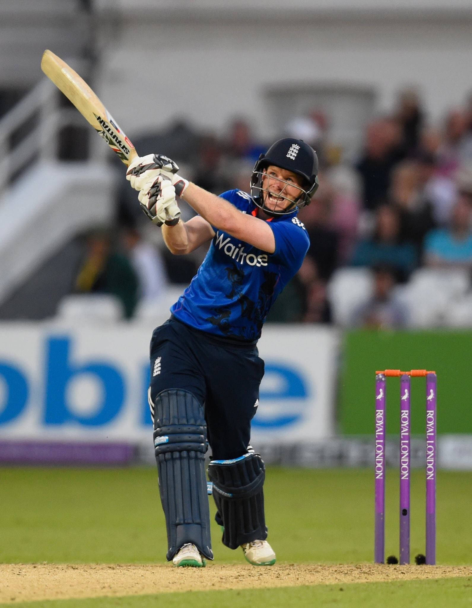 eoin morgan 桌布 壁紙 — 一名身穿藍色球衣的板球擊球手在夜間比賽中，在球場燈光下強力揮棒擊球。