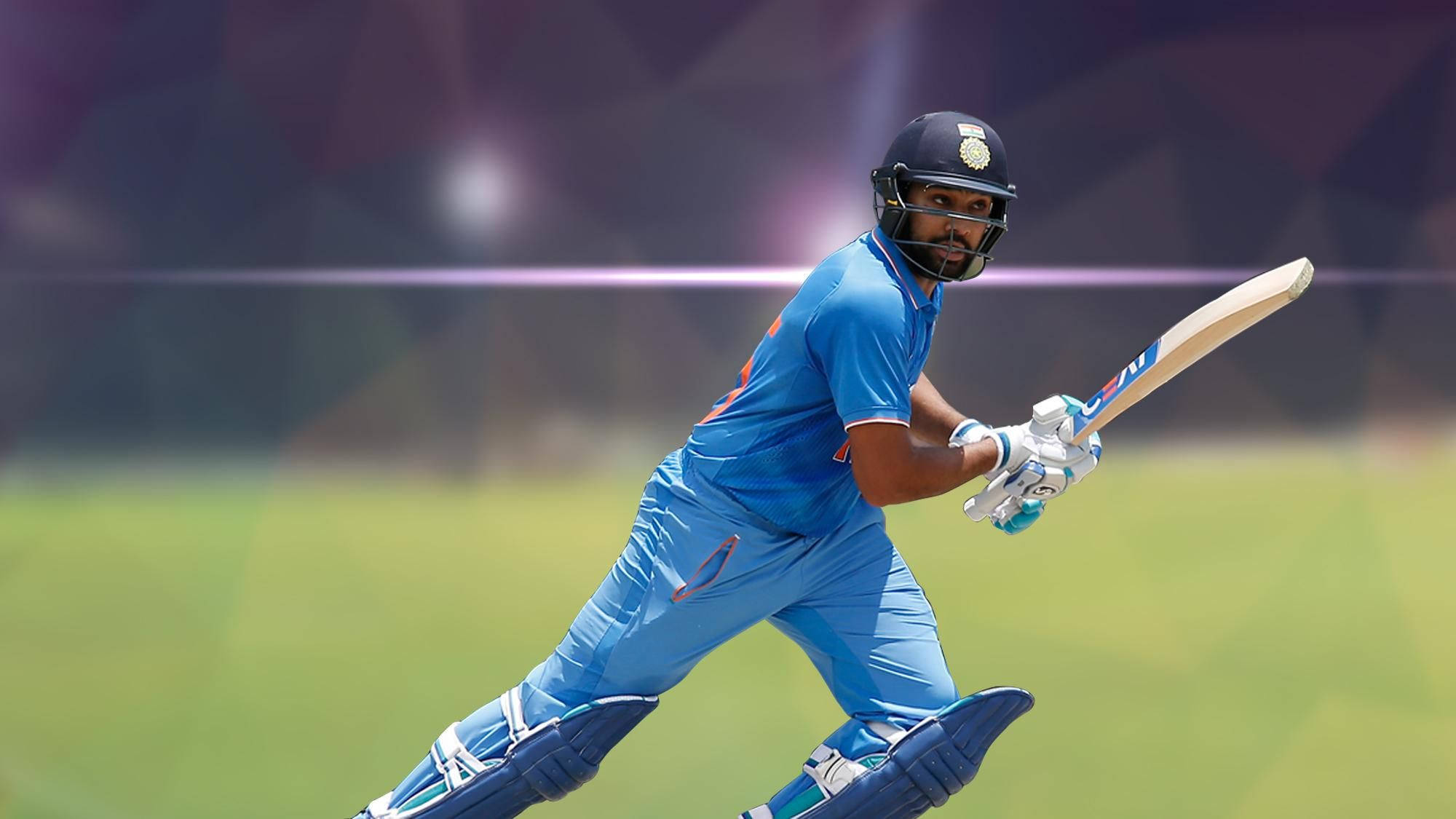 Rohit Sharma 桌布 壁紙 — 一名身穿藍色球衣的板球擊球手在陽光明媚的綠色球場上揮動球棒，背景是模糊的體育場燈光。