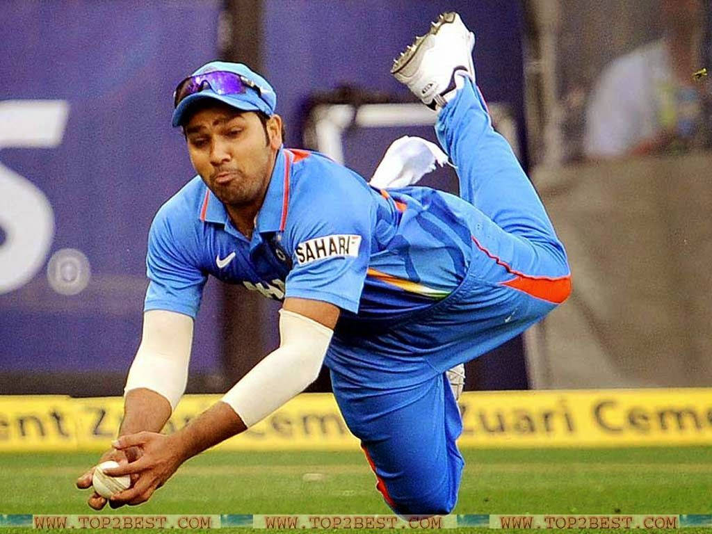 Rohit Sharma 桌布 壁紙 — 一名身穿藍色球衣的板球運動員在球場燈光下，在綠色場地上動態飛身接球。
