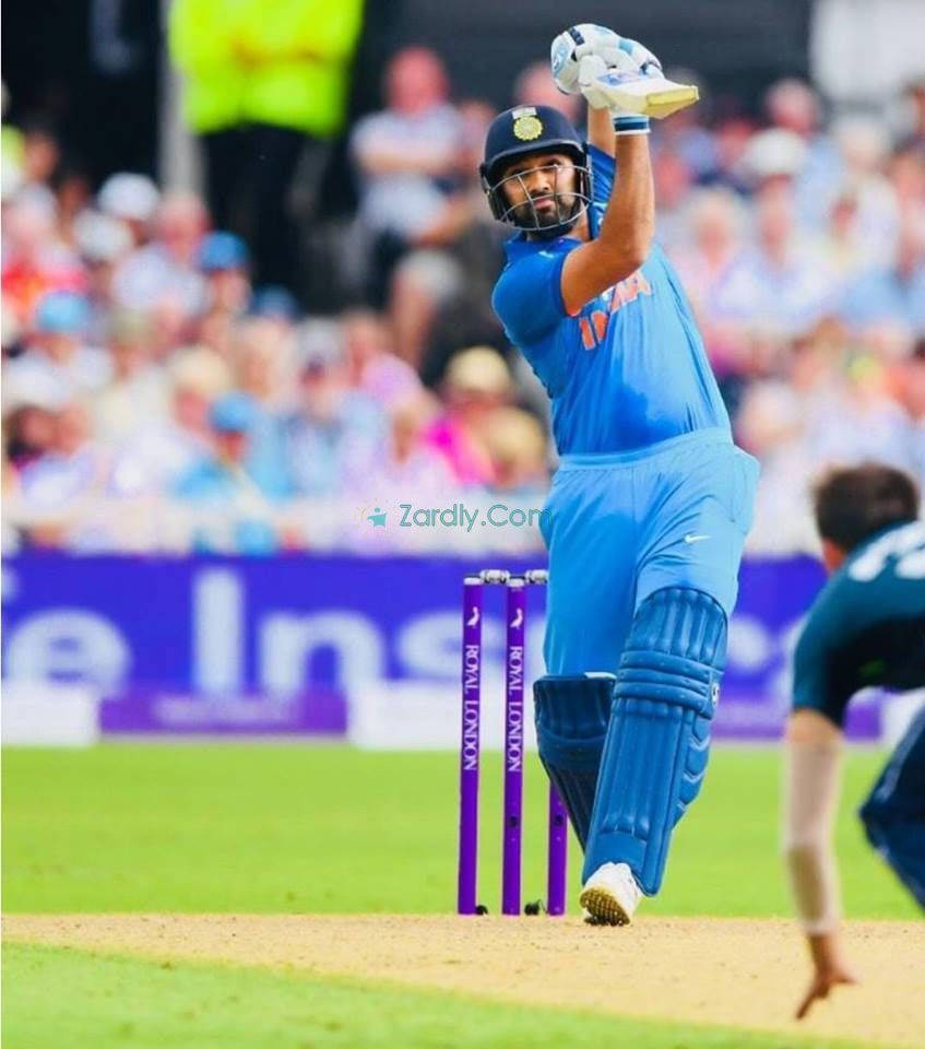 Rohit Sharma 桌布 壁紙 — 一名身穿藍色球衣的板球運動員在陽光明媚的綠色球場上高舉球棒，慶祝一次強力擊球。