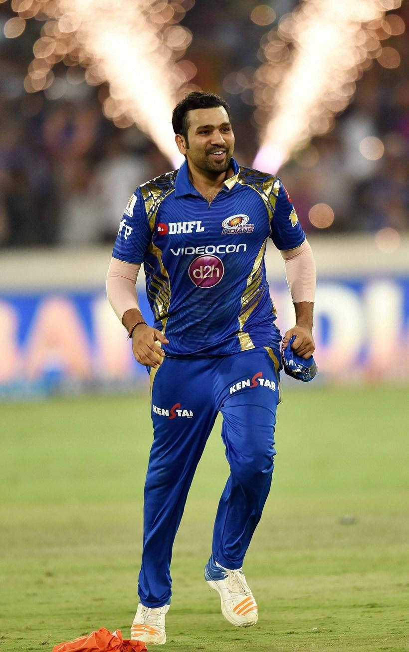 Mumbai Indians 桌布 壁紙 — 一名身穿藍色球衣的板球運動員微笑著跑過體育場，身後有煙火綻放。