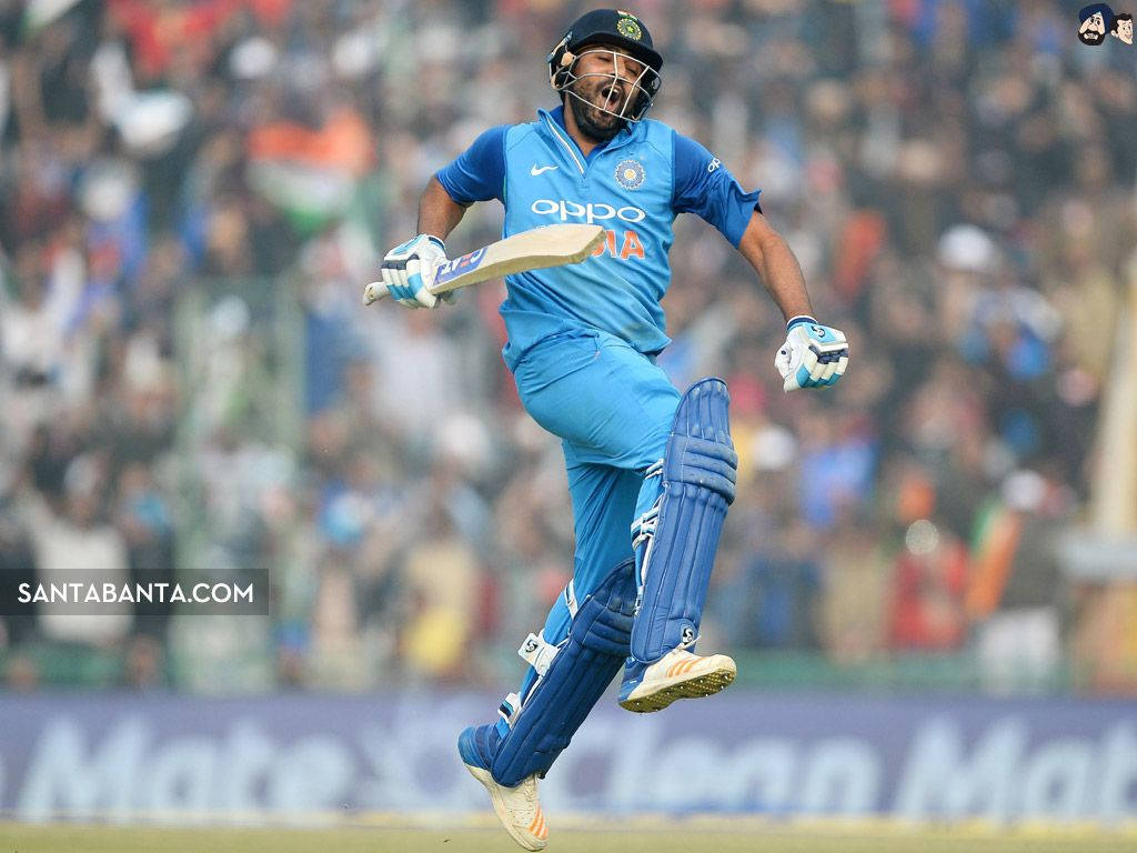 Rohit Sharma 桌布 壁紙 — 一名身穿藍色球衣的板球選手在歡呼的人群面前擊出邊界球後，手持球拍愉快地躍起空中。