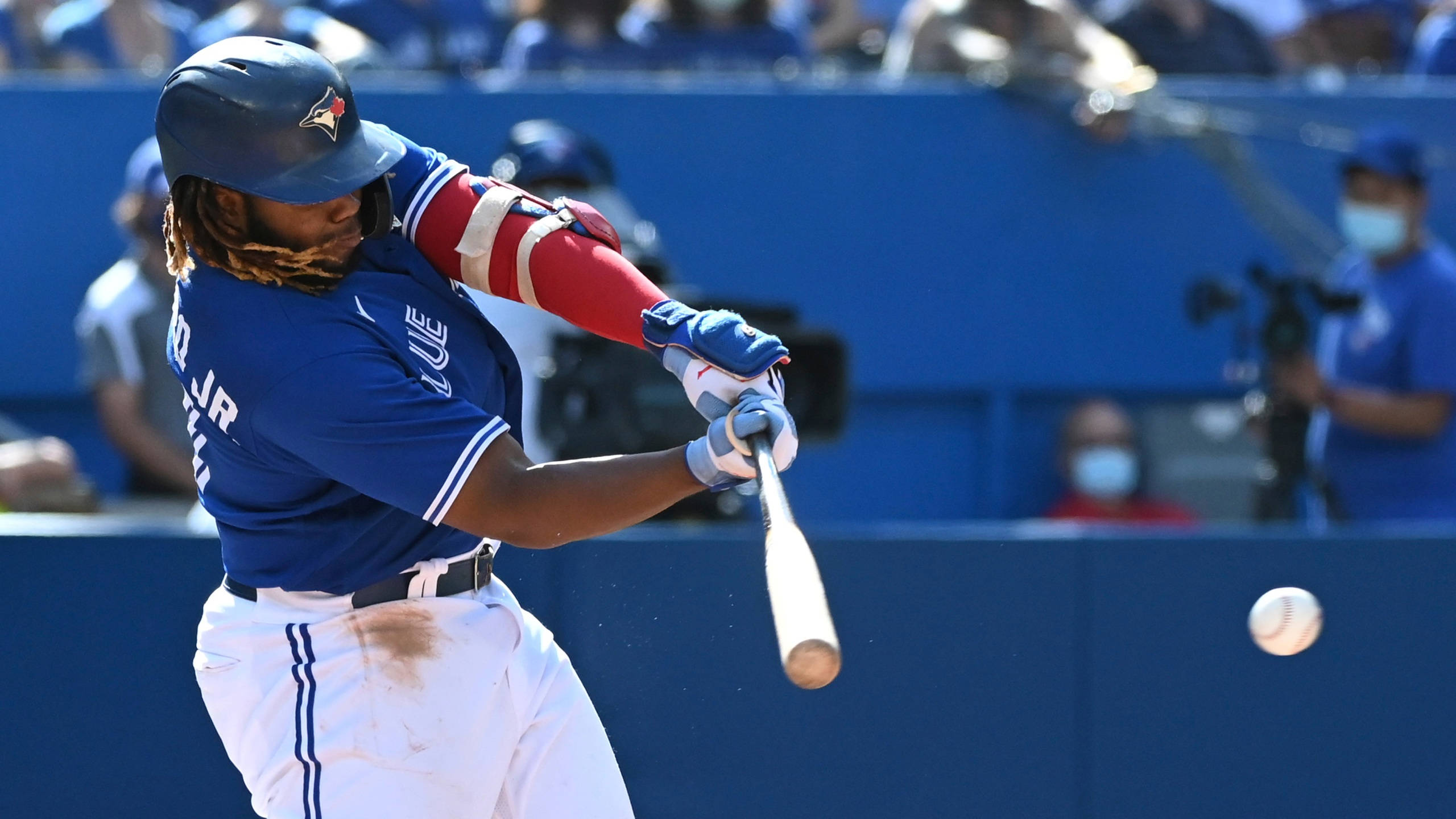 Vladimir 桌布 壁紙 — 一名身穿藍色球衣的棒球運動員在明亮的日間比賽中揮棒擊球，背景有觀眾。