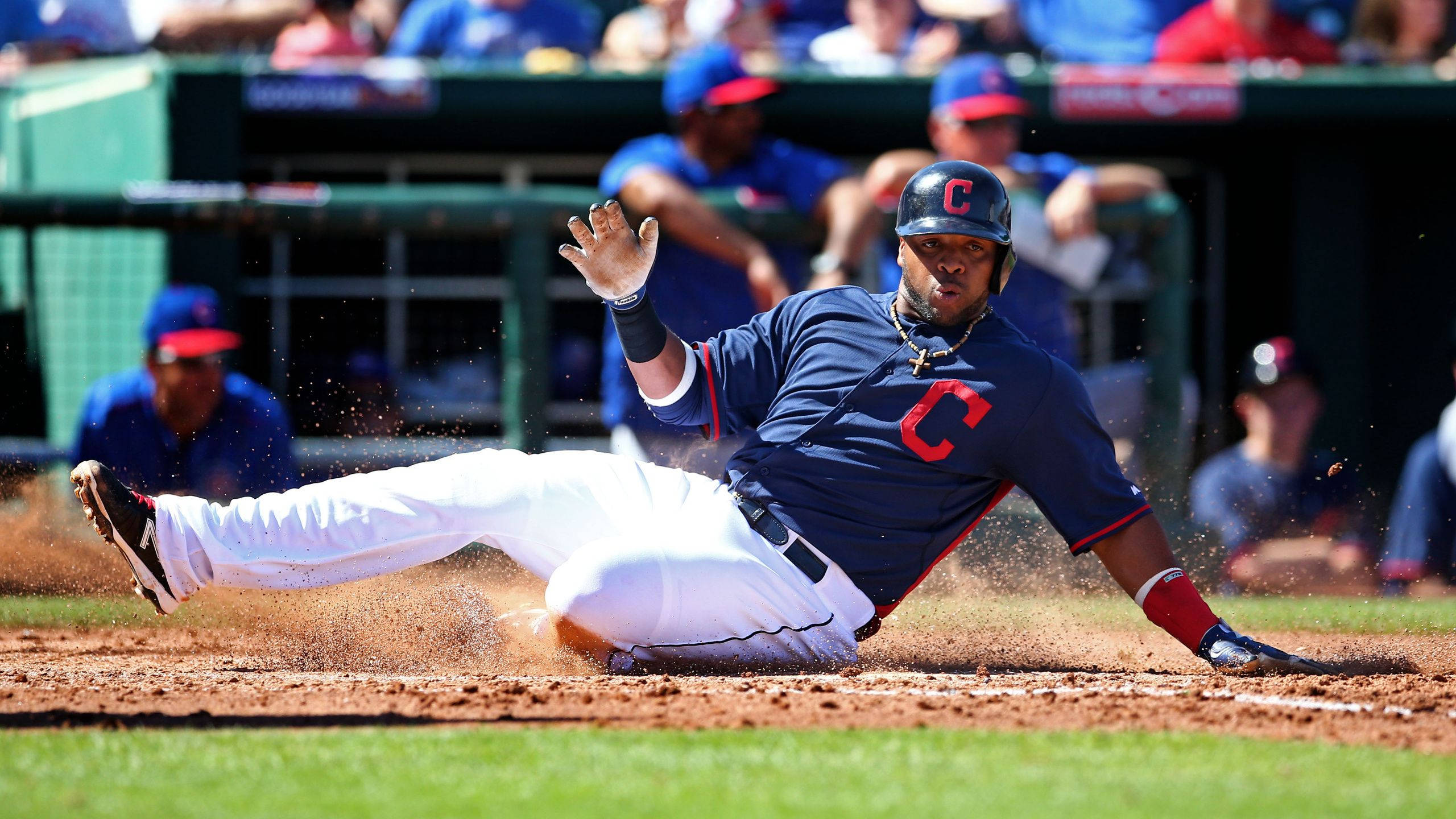 Cleveland Indians 桌布 壁紙 — 一名身穿藍色球衣的棒球運動員在明亮的日光下頭部先滑進本壘板，揚起泥土。