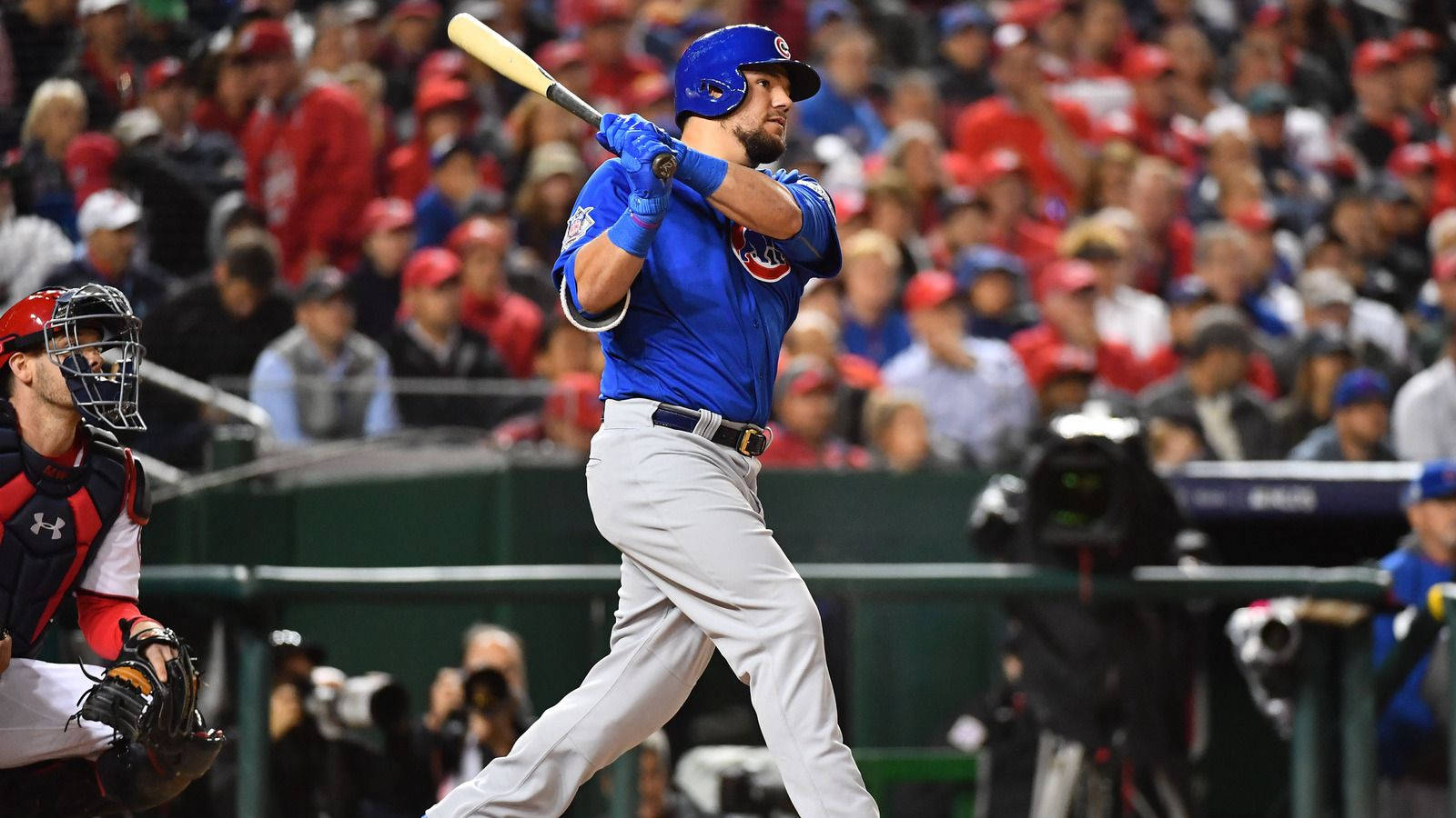 Chicago Cubs 桌布 壁紙 — 一名身穿藍色球衣的棒球運動員在本壘板揮棒，背景有捕手和觀眾。