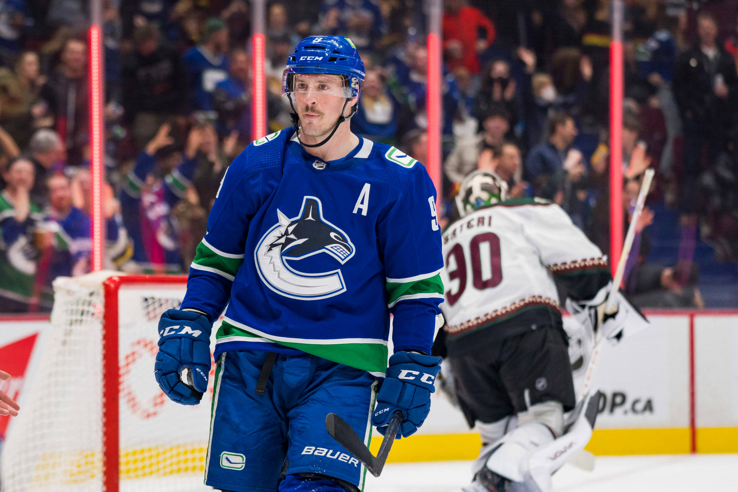 Vancouver 桌布 壁紙 — 一名身穿藍色球衣的溫哥華加人隊（Vancouver Canucks）冰球運動員在冰上走近球門，背景有觀眾。