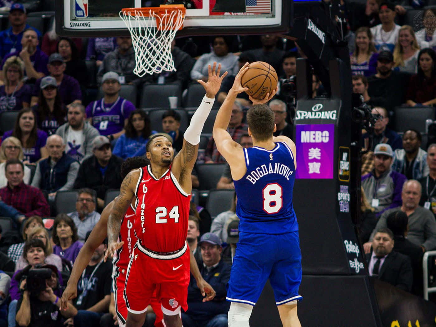 NBA 桌布 壁紙 — 一名身穿藍色球衣的籃球運動員向籃框投籃，一名身穿紅色球衣的防守球員跳起封阻，比賽在座無虛席的場館內進行。