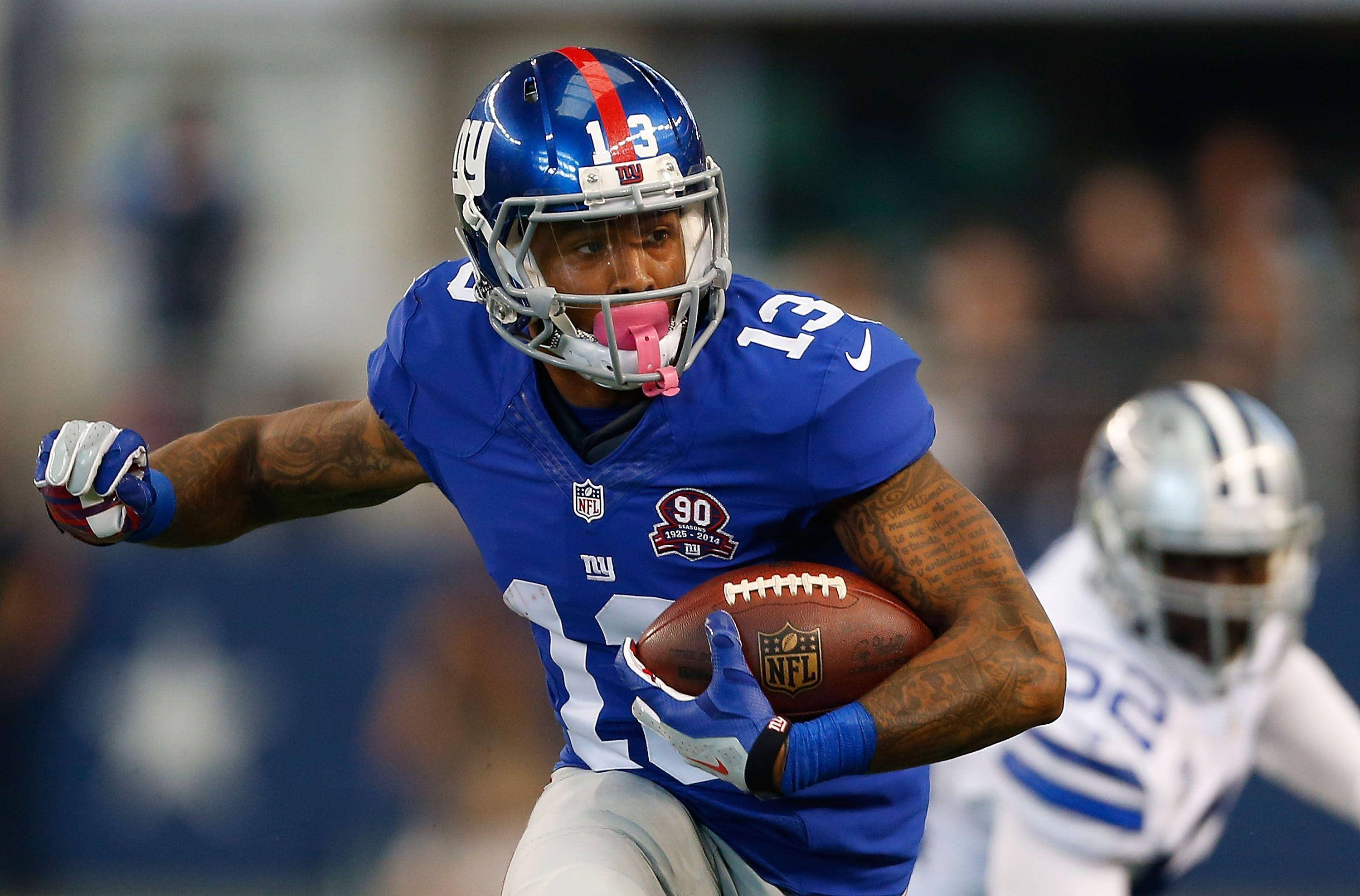 Odell 桌布 壁紙 — 一名身穿藍色球衣的紐約巨人隊美式足球員在比賽中帶球奔跑，背景有模糊的對手。
