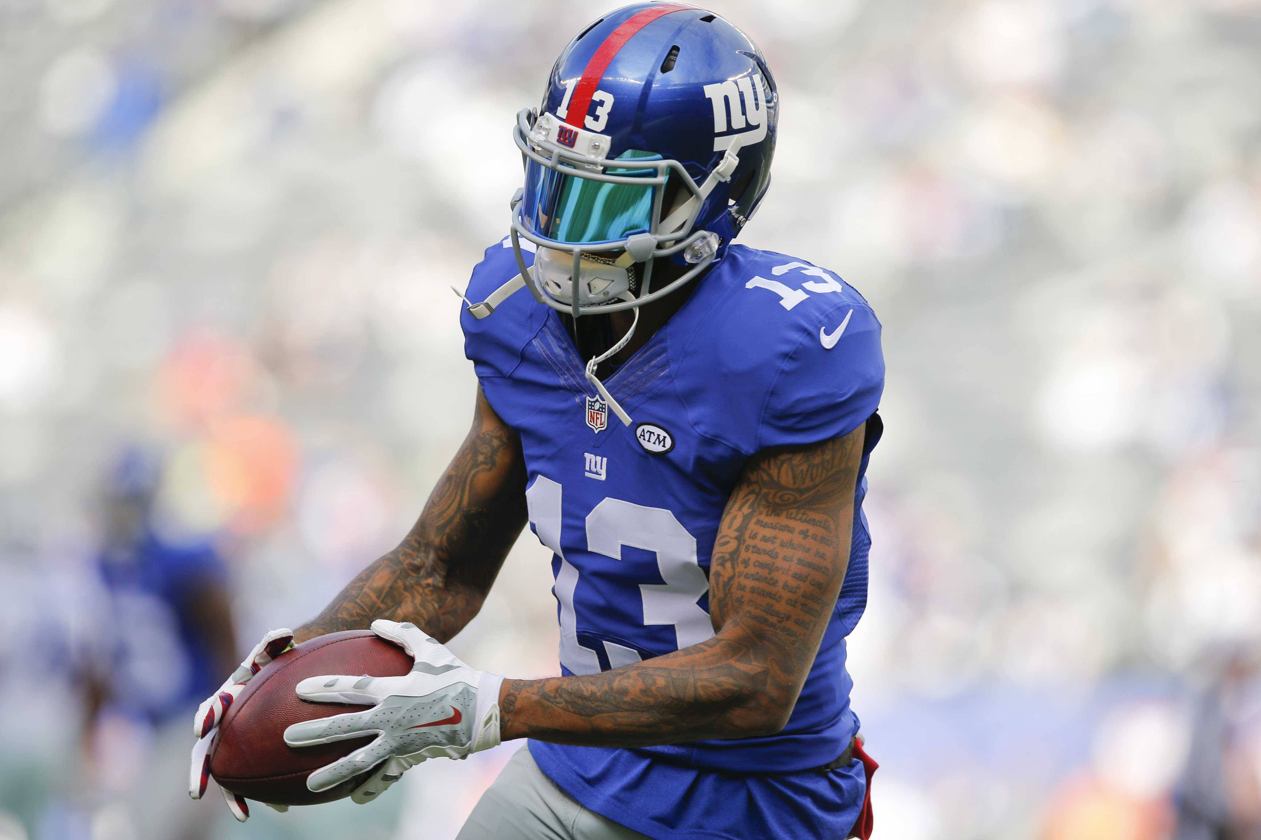 Odell 桌布 壁紙 — 一名身穿藍色球衣的紐約巨人隊美式足球員在日間比賽中帶球奔跑，背景是模糊的體育場。