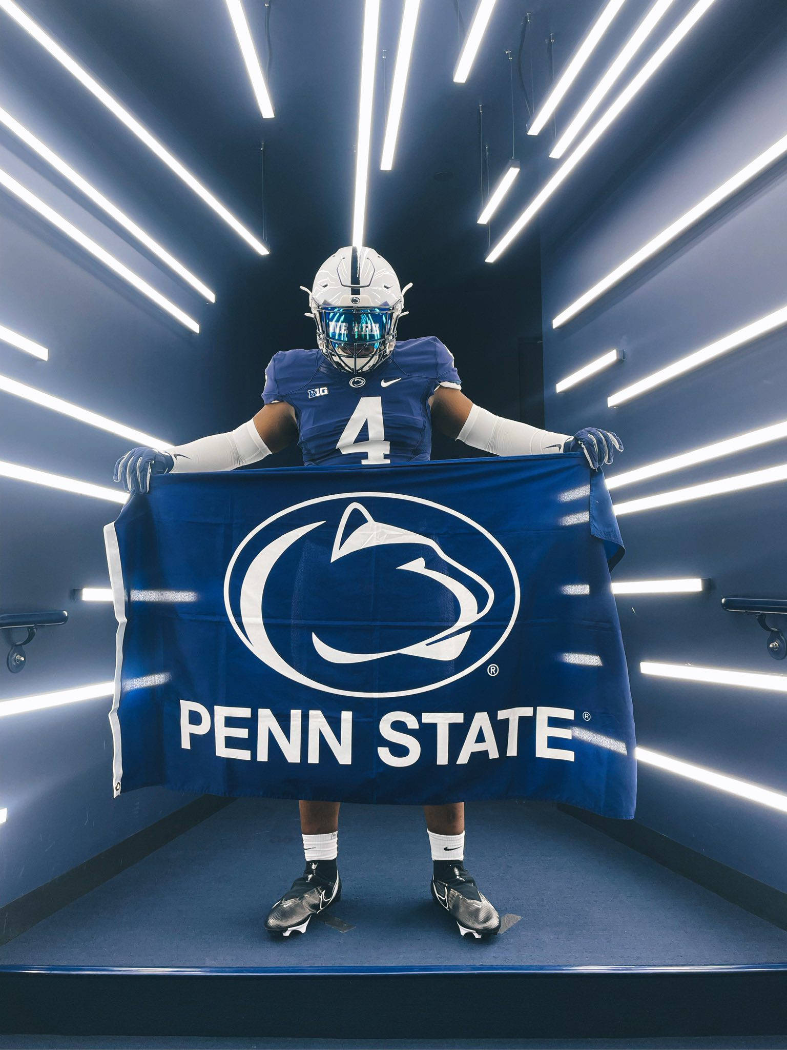 Penn State 桌布 壁紙 — 一名身穿藍色球衣的賓夕法尼亞州立大學美式足球運動員在明亮的白色隧道燈光下手持隊旗。