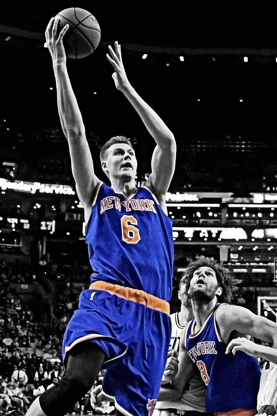 Kristaps Porzingis 桌布 壁紙 — 一名身穿藍色紐約球衣的籃球運動員跳起投籃，防守球員伸手阻擋，高對比度的黑白球館場景。