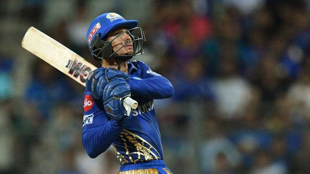 Mumbai Indians 桌布 壁紙 — 一名身穿藍色裝備的板球擊球手在模糊的體育場人群中高舉球棒慶祝勝利。