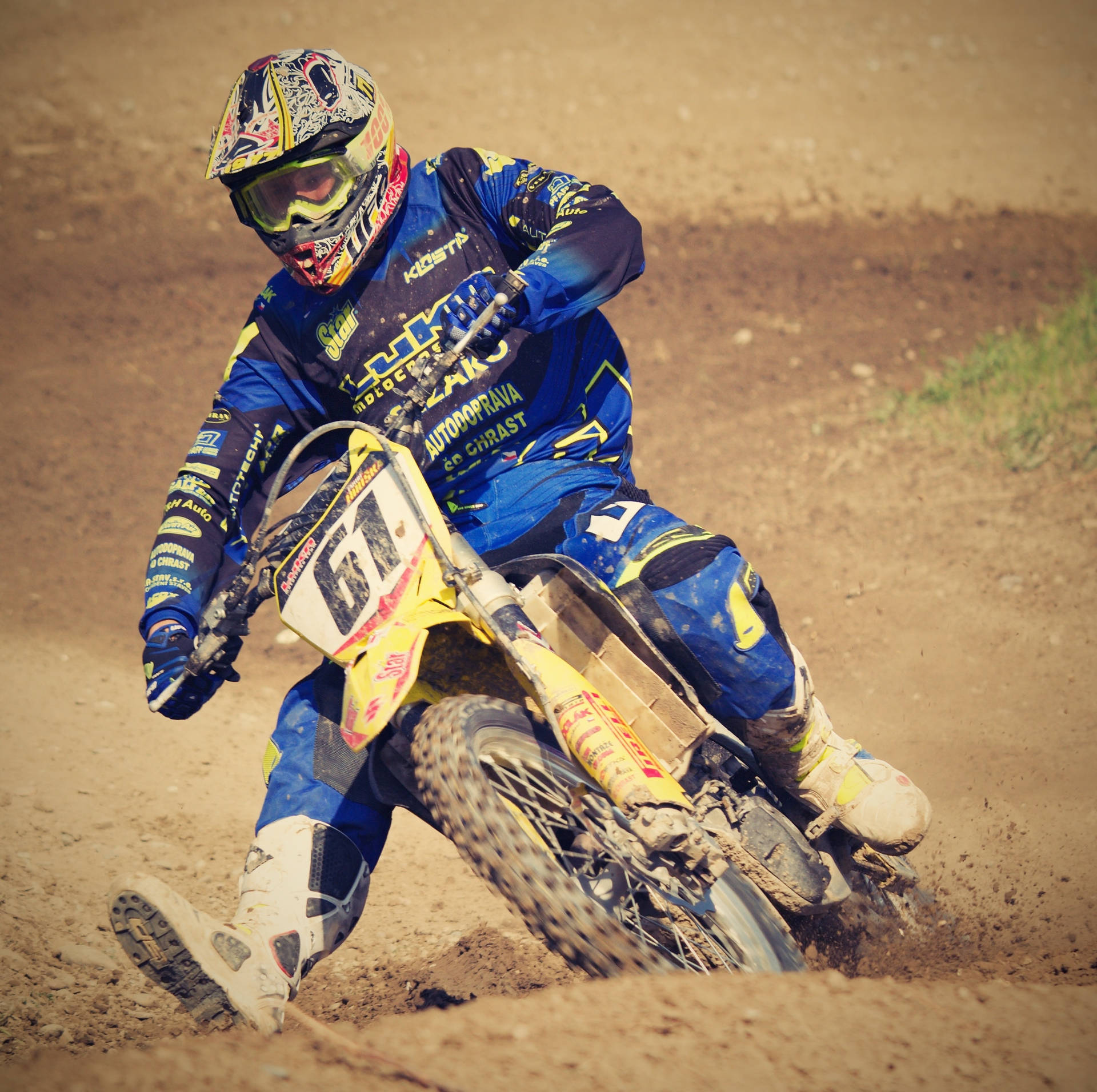 Motocross 桌布 壁紙 — 一名身穿藍色裝備的越野摩托車手在陽光普照的泥地上傾斜入彎，揚起塵土。