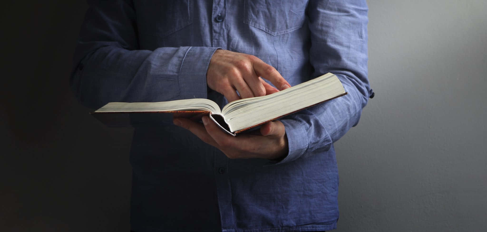 Bible Study 桌布 壁紙 — 一名身穿藍色襯衫的人，雙手輕輕放在打開的書頁上，背景為柔和的灰色。