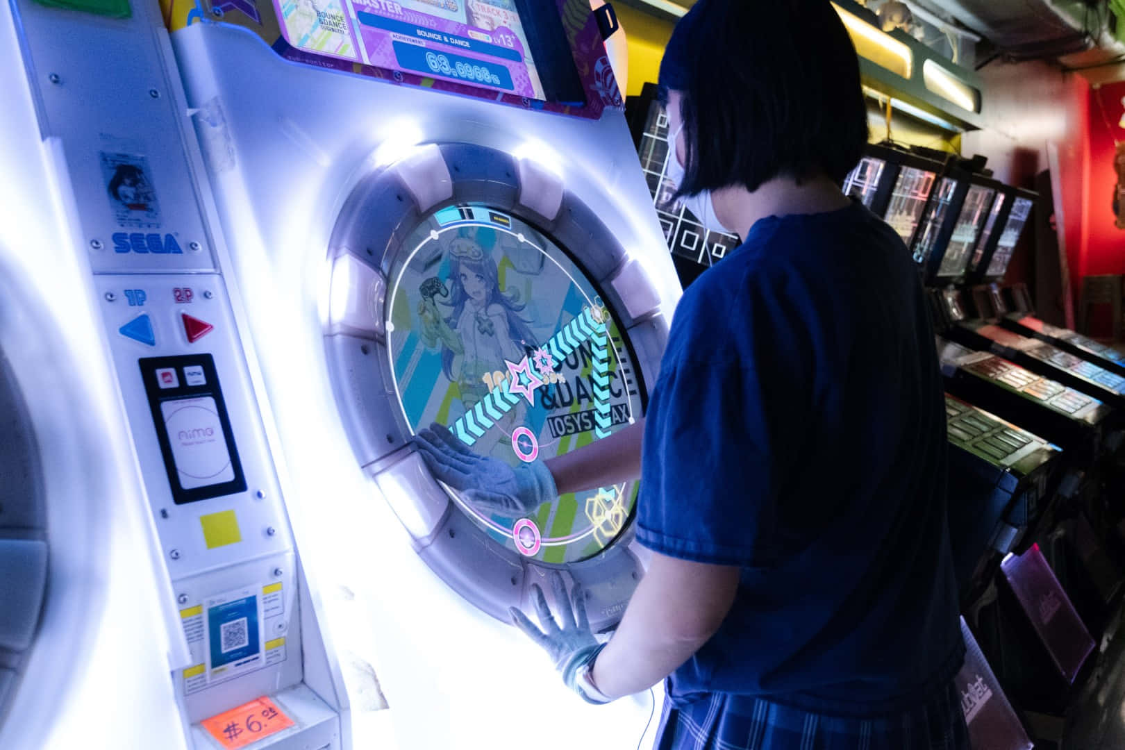 Arcade Games 桌布 壁紙 — 一名身穿藍色襯衫的人在燈光昏暗的遊戲機中心玩著一款發光的Sega街機遊戲，遊戲帶有色彩繽紛的動畫圖形。