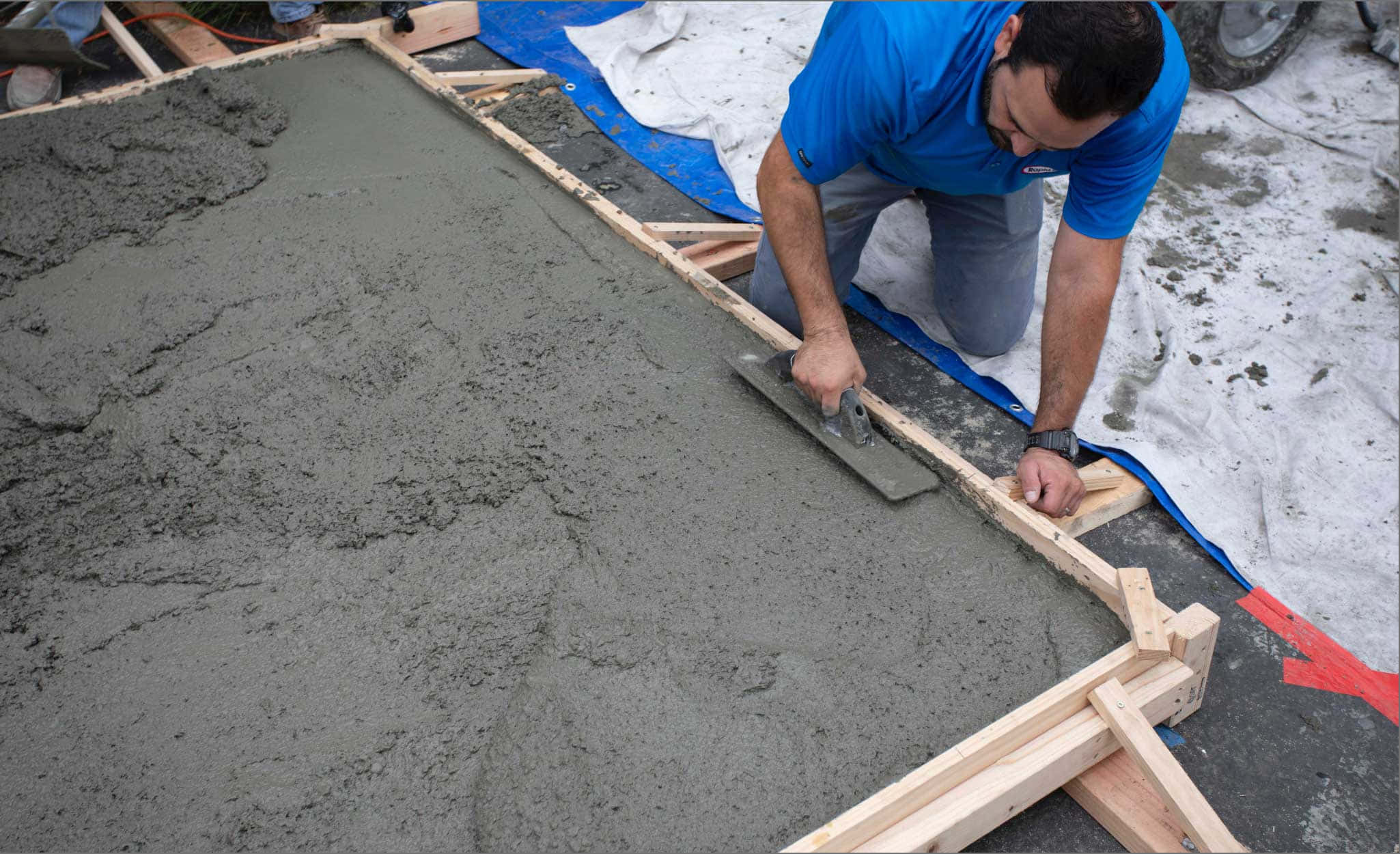 混凝土 桌布 壁紙 — 一名身穿藍色襯衫的建築工人在雪地上小心地將木模板內的濕混凝土抹平。