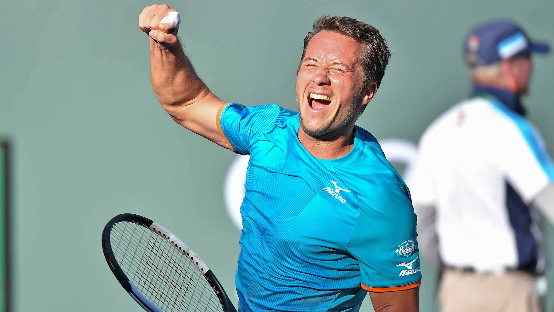 網球 桌布 壁紙 — 一名身穿藍色襯衫的男網球運動員高舉拳頭，歡呼勝利，同時握著球拍。