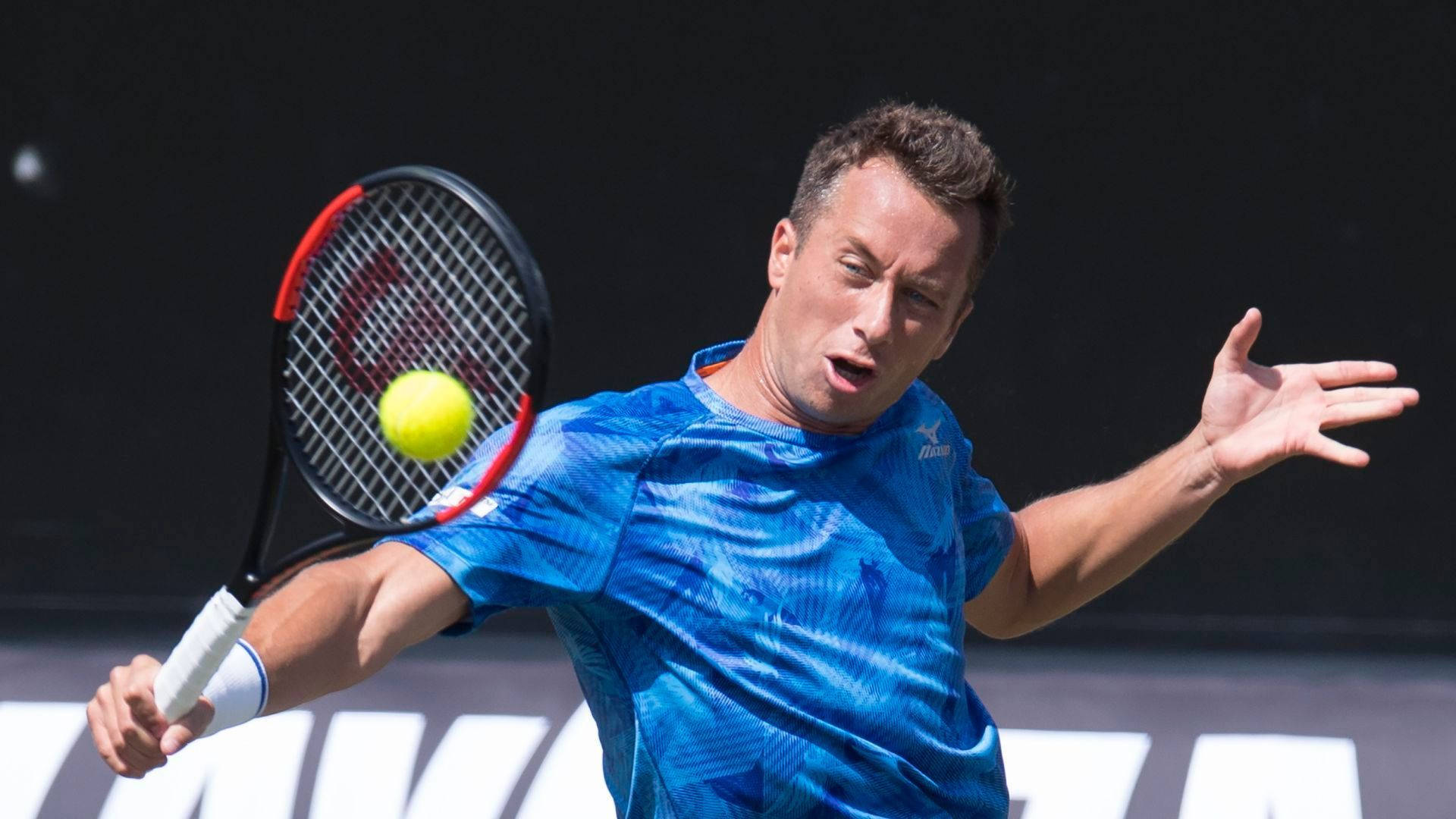 Tennis 桌布 壁紙 — 一名身穿藍色襯衫的男網球選手在深色背景下揮動球拍擊打黃色球。