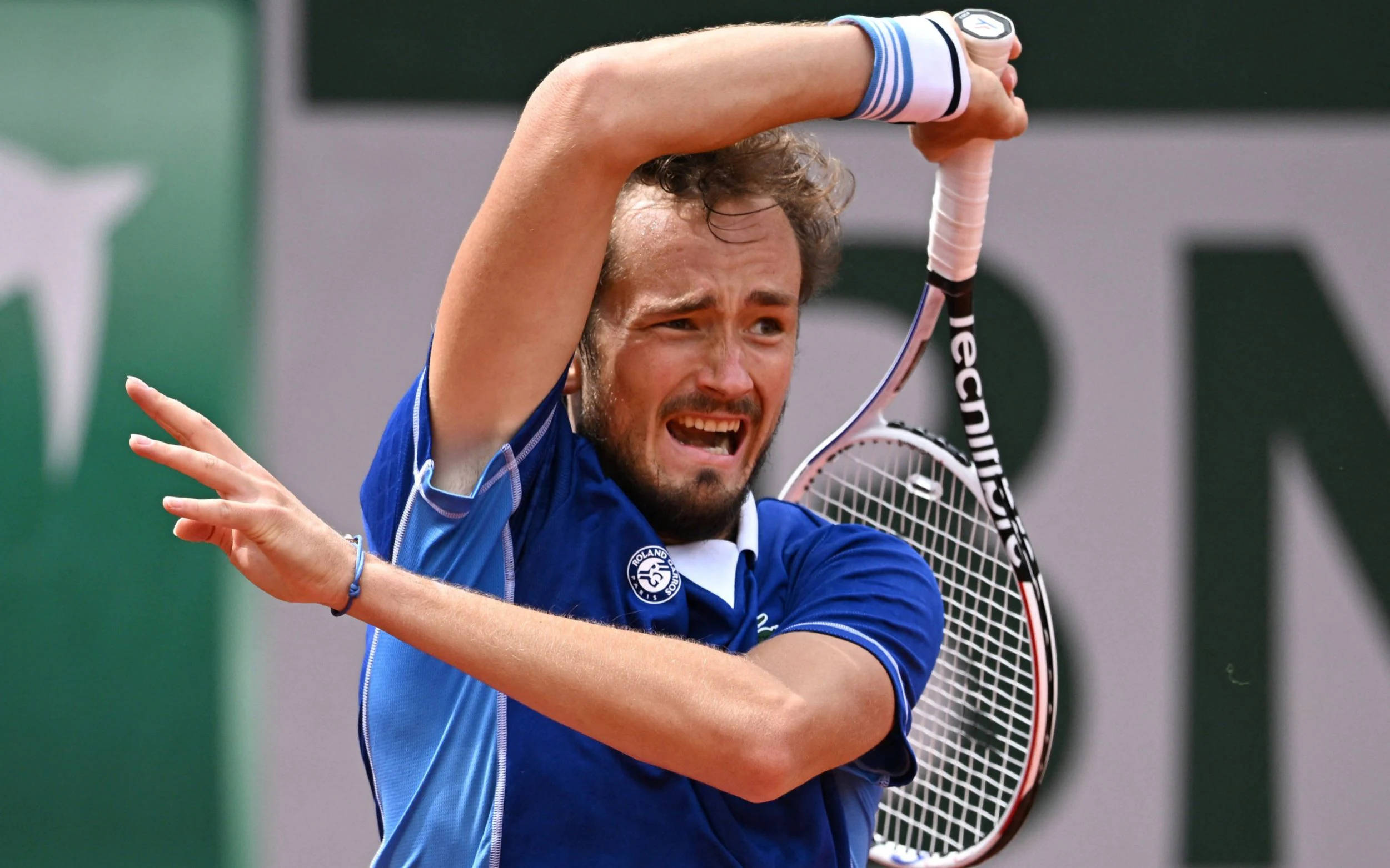 Tennis 桌布 壁紙 — 一名身穿藍色襯衫的男網球選手在紅土球場上揮拍，表情猙獰，專注力極強。
