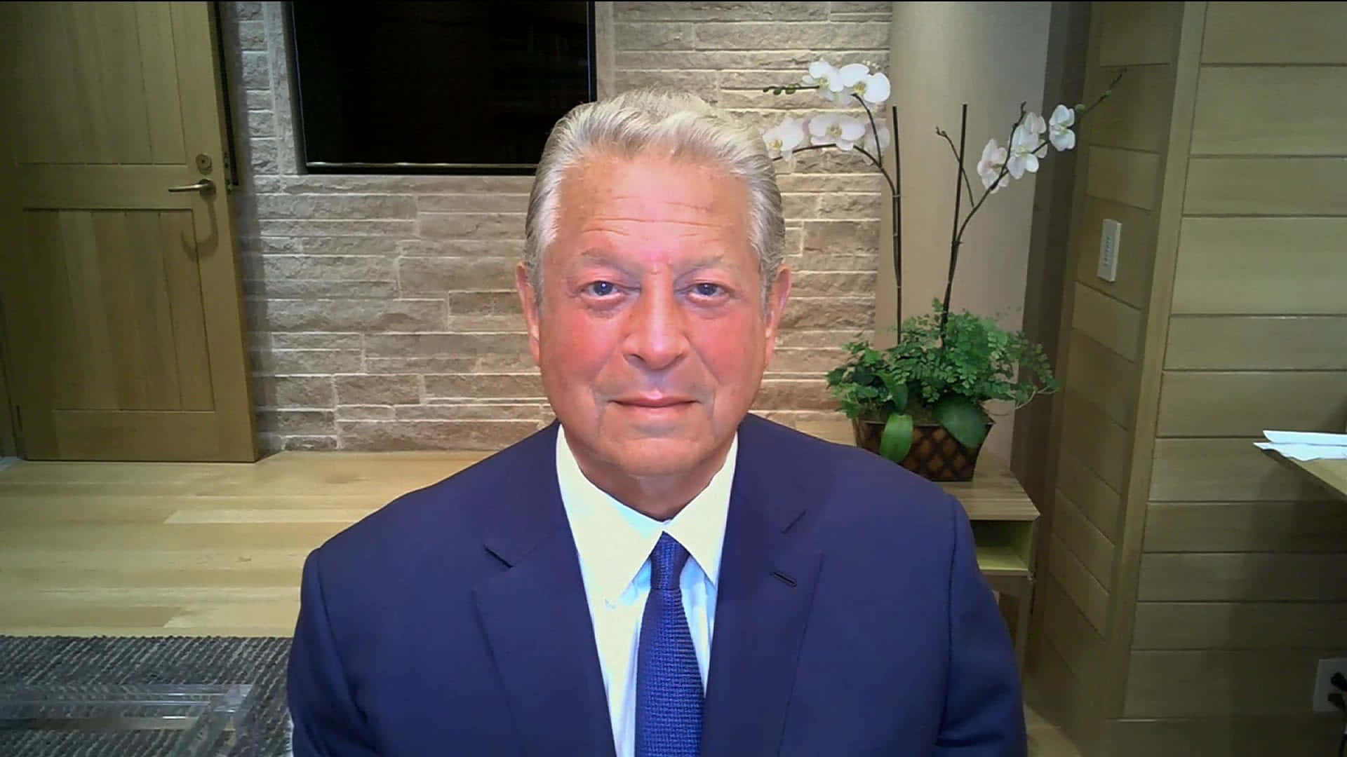 Celebrity 桌布 壁紙 — 一名身穿藍色西裝及領帶的男子在室內靠著石牆而坐，旁邊有白色蘭花和木門。
