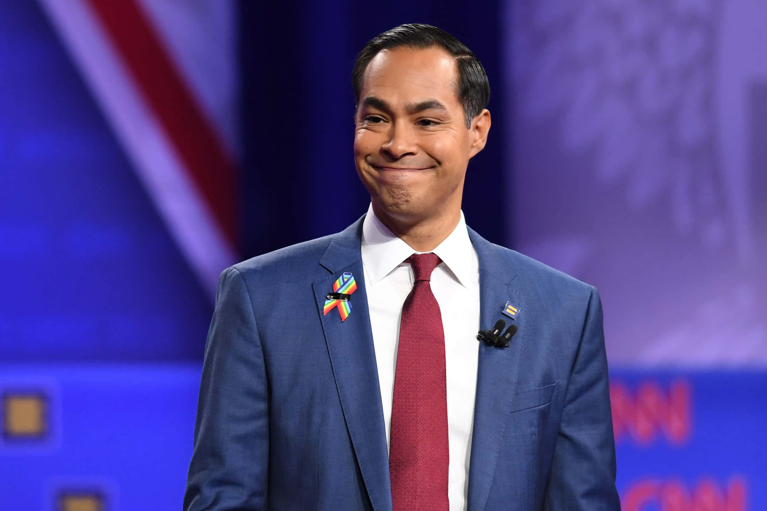 Celebrity 桌布 壁紙 — 一名身穿藍色西裝和紅色領帶的男子在CNN舞台上佩戴彩虹別針，露出溫暖的笑容。