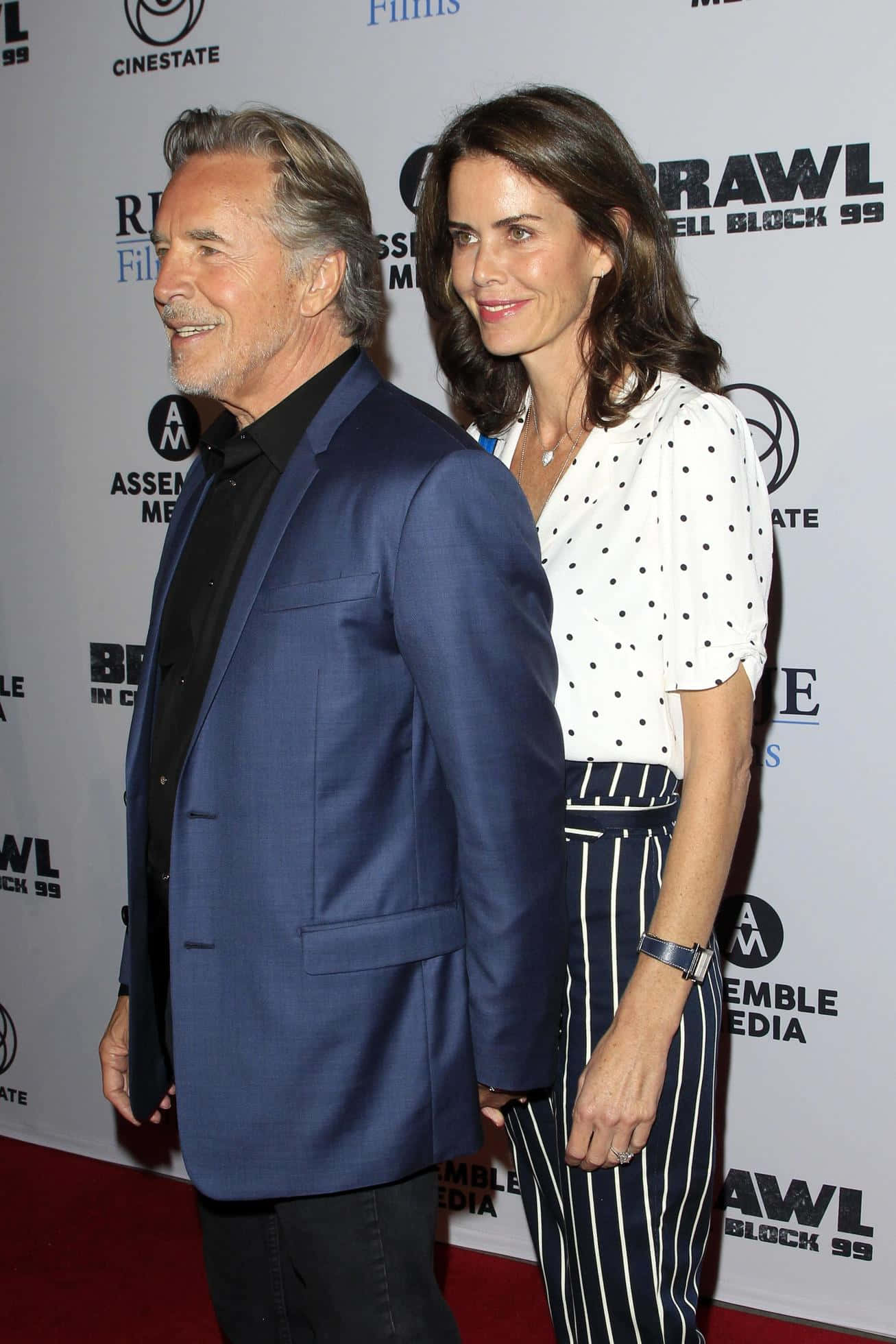 Don Johnson 桌布 壁紙 — 一名身穿藍色西裝的男子和一名身穿波點襯衫的女子在電影首映禮的紅地毯上微笑站立。