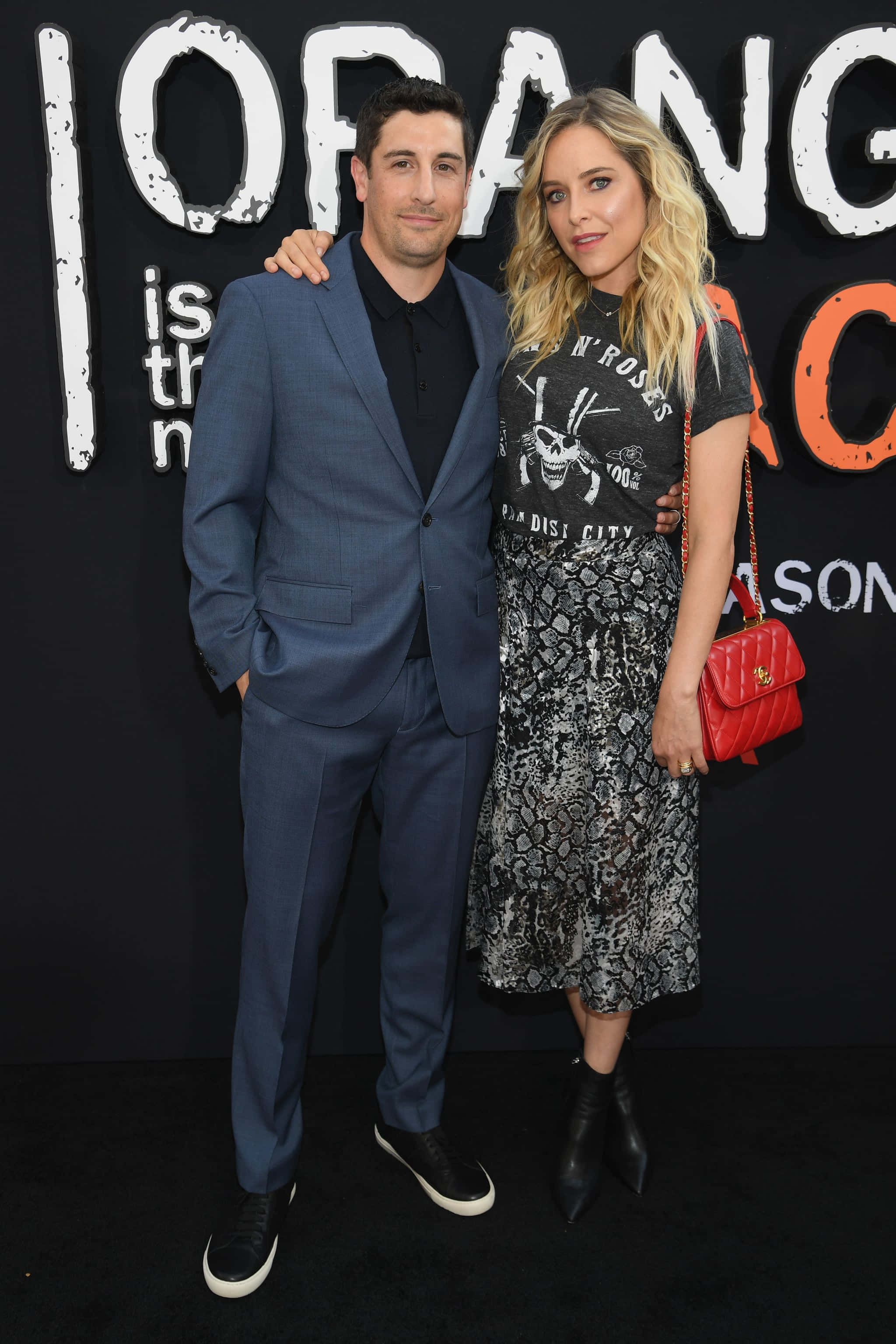 Jason Biggs 桌布 壁紙 — 一名身穿藍色西裝的男子和一名身穿圖案連衣裙的女子在Orange Is the New Black活動中，以大膽的背景一起擺姿勢。