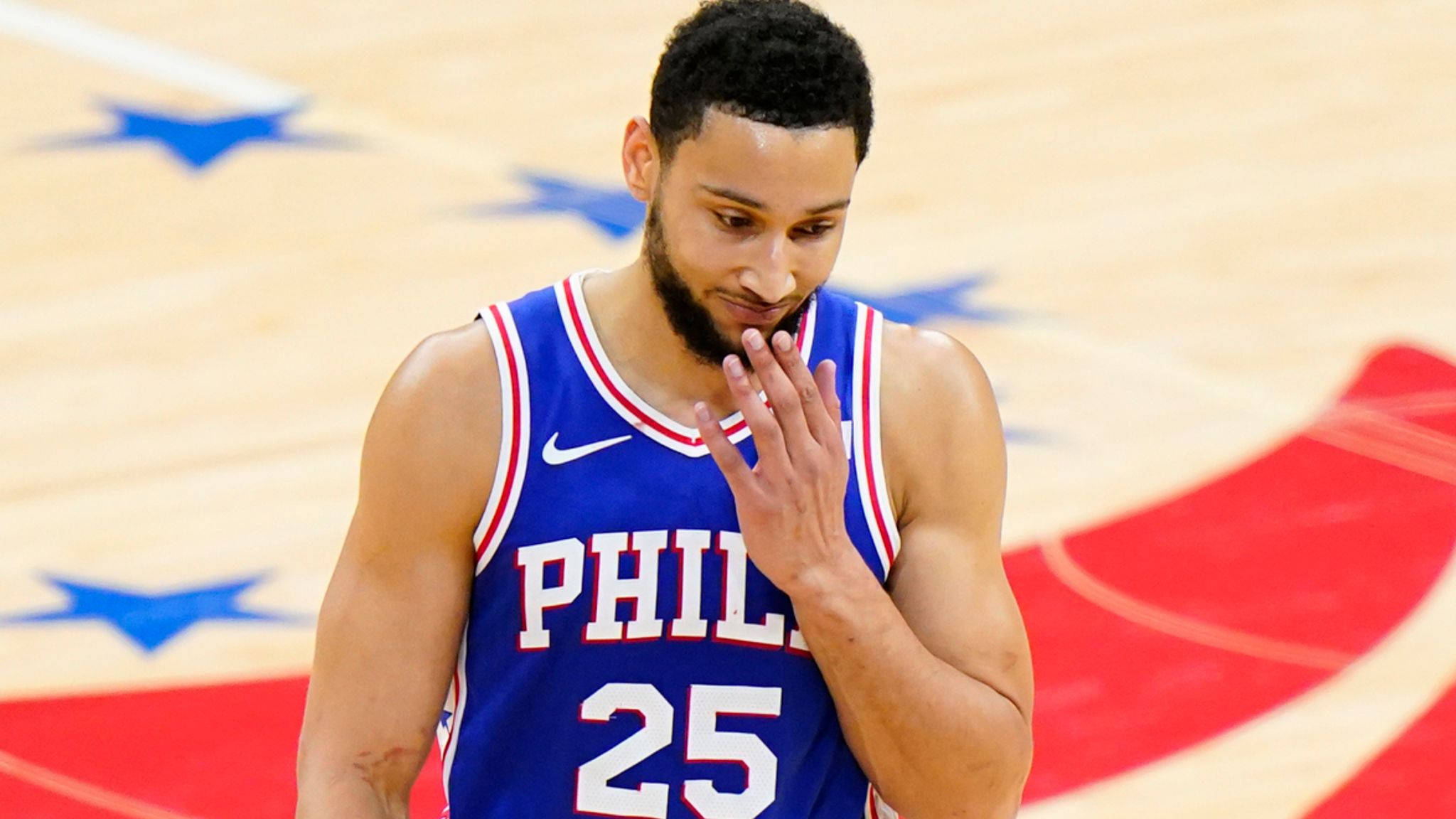 76ers 桌布 壁紙 — 一名身穿藍色費城25號球衣的籃球運動員在紅藍星形圖案的球場上用手摀住嘴巴。