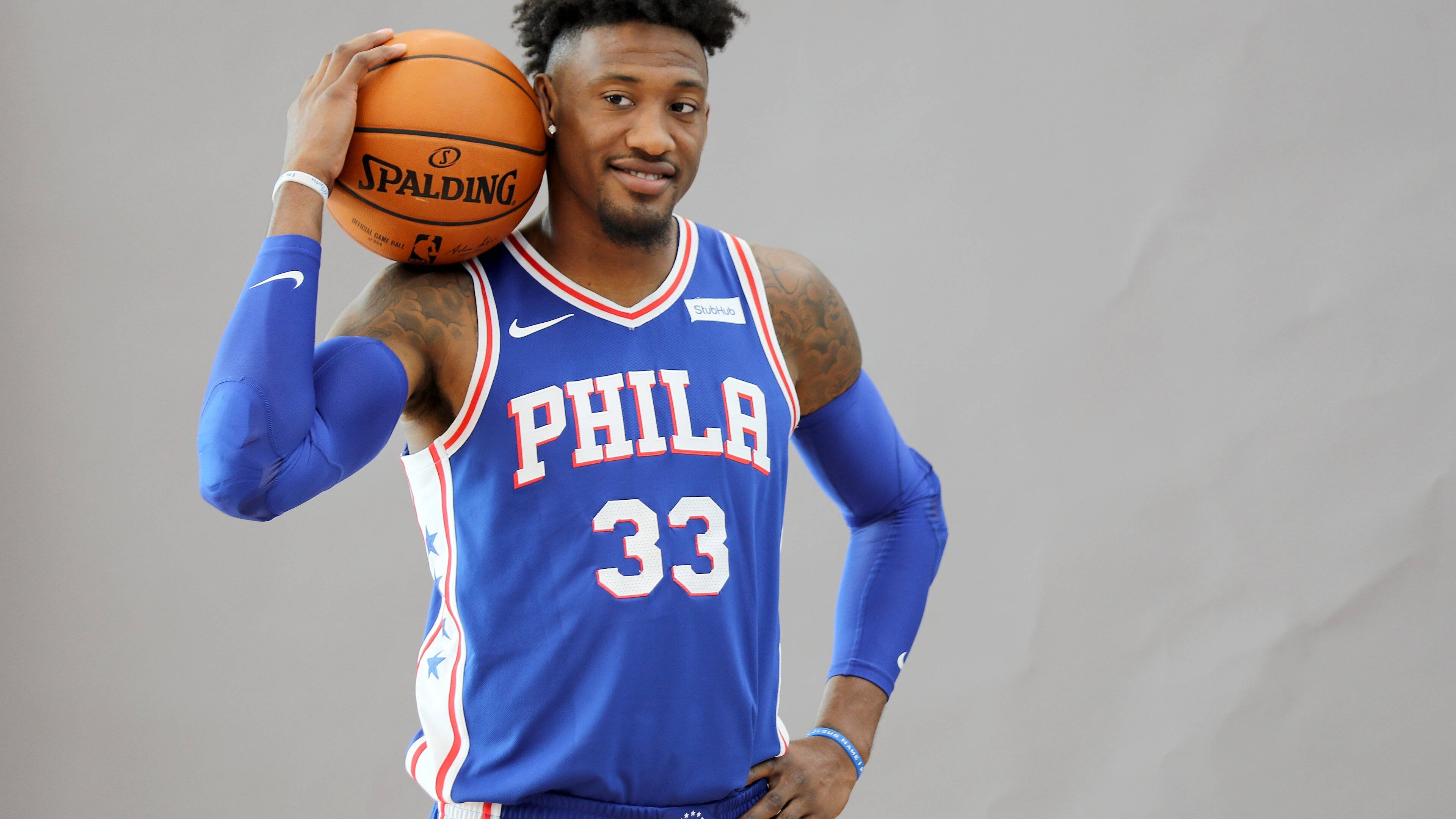 robert covington 桌布 壁紙 — 一名身穿藍色費城76人球衣的籃球運動員，在純灰色工作室背景前手持Spalding籃球。