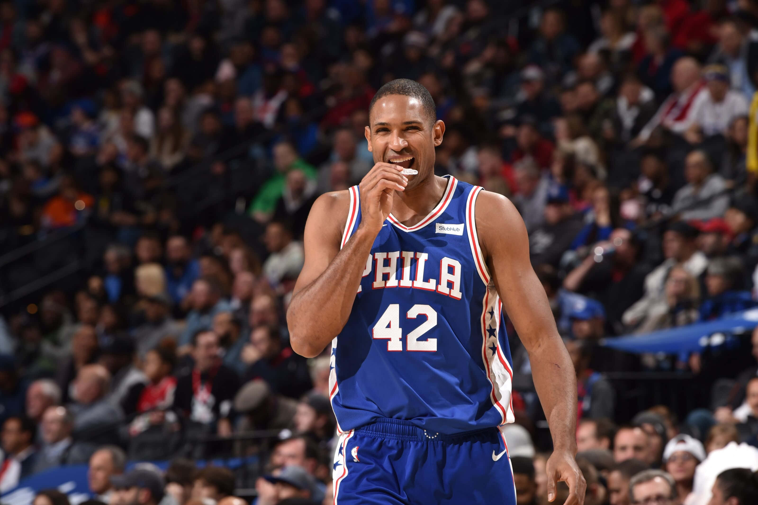 Al Horford 桌布 壁紙 — 一名身穿藍色費城76人隊42號球衣的籃球運動員在比賽中咬著手指微笑。