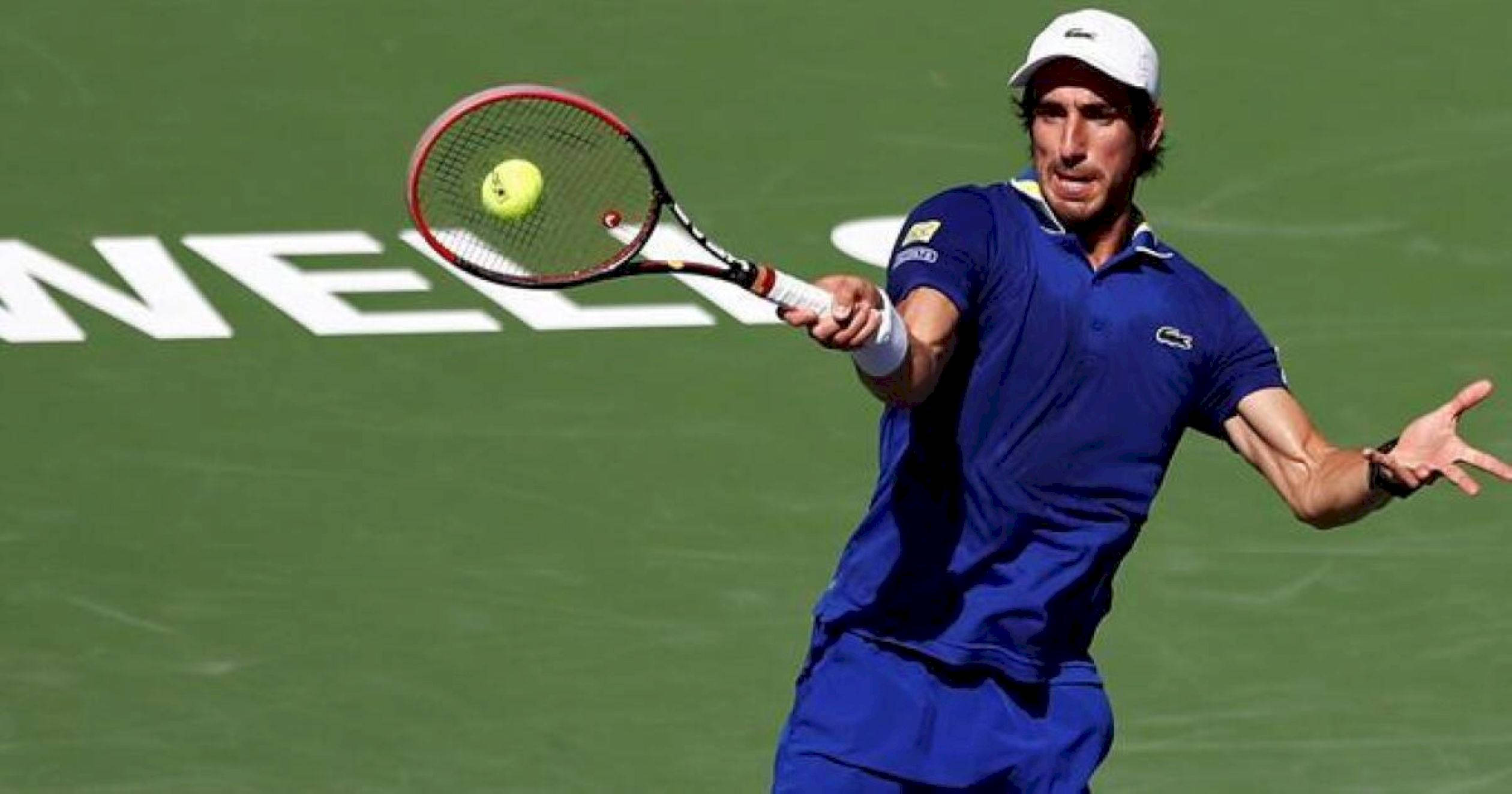 Athletic 桌布 壁紙 — 一名身穿藍色運動服的男網球選手在明亮的日光下，於綠色球場揮拍擊打黃色網球。