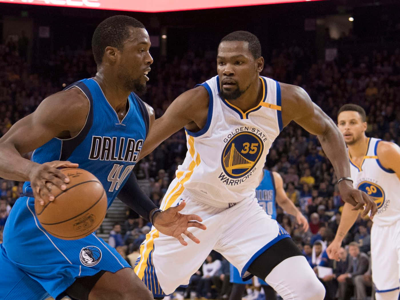 NBA 桌布 壁紙 — 一名身穿藍色達拉斯球衣的籃球運動員在運球時，被一名身穿白色和黃色的金州勇士隊球員緊密防守。