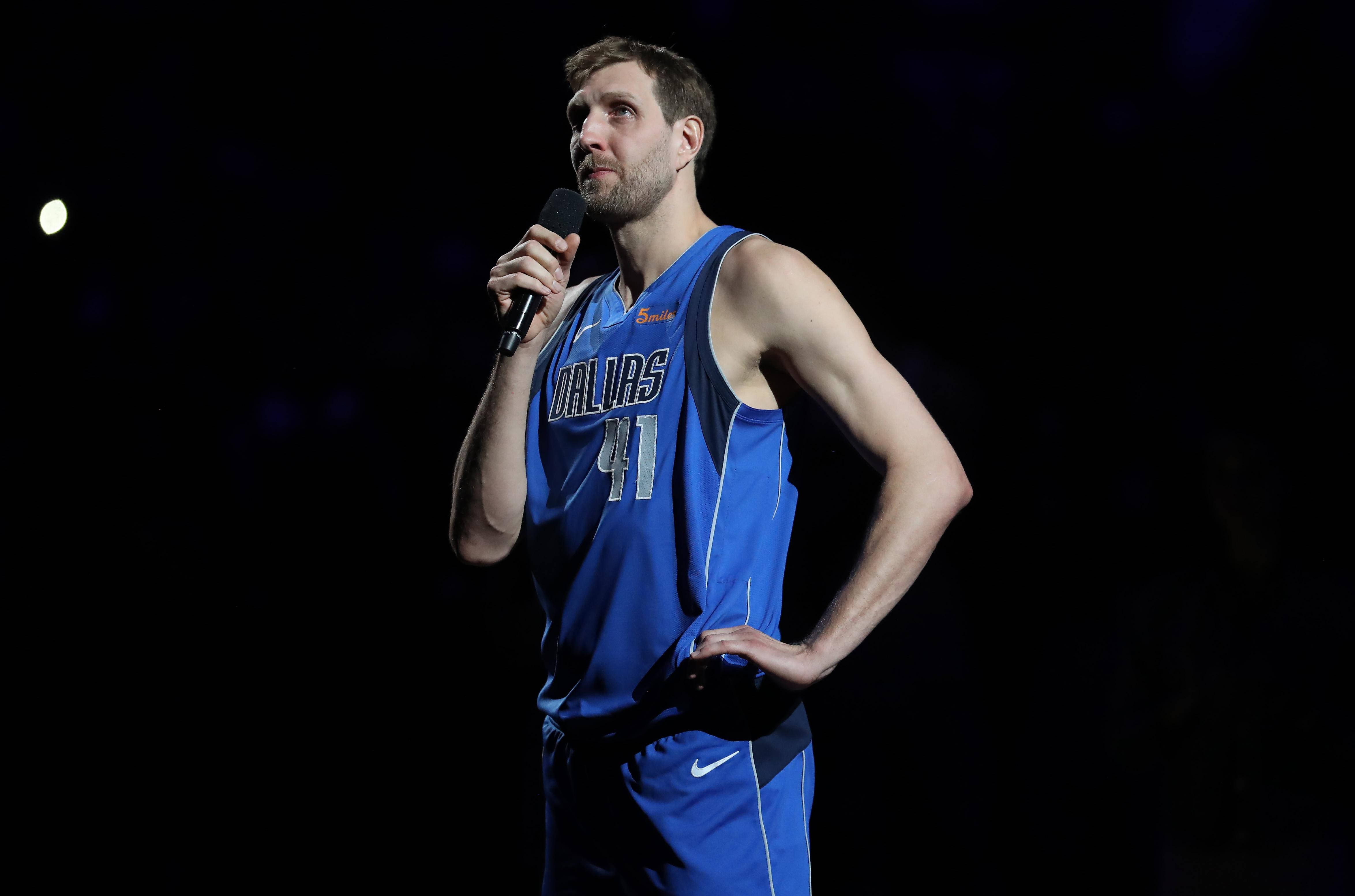 Dirk Nowitzki 桌布 壁紙 — 一名身穿藍色達拉斯球衣的籃球運動員在黑暗的舞台背景和聚光燈下拿著麥克風。