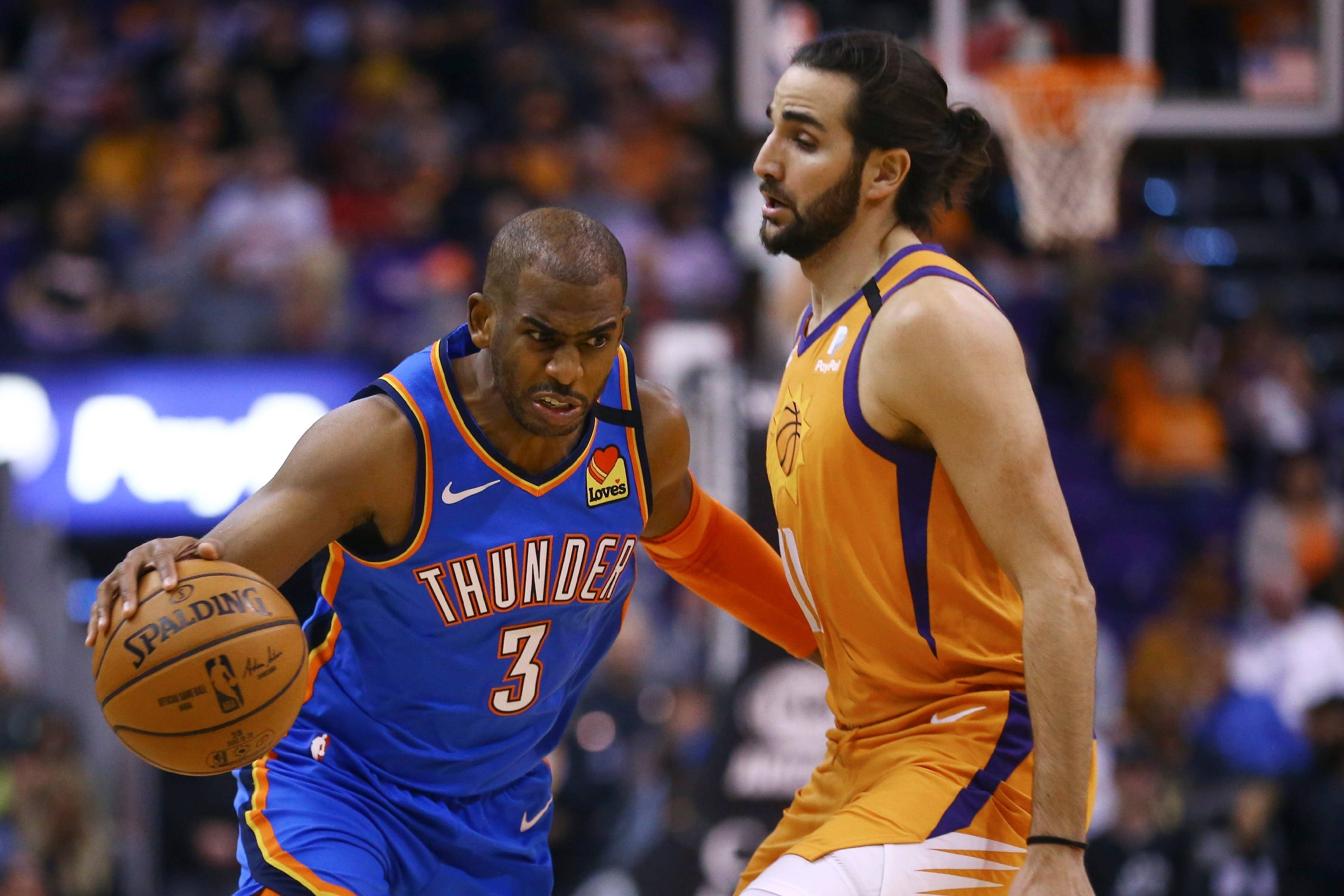 Ricky Rubio 桌布 壁紙 — 一名身穿藍色雷霆隊球衣的籃球運動員在比賽中運球，同時被一名身穿橙色太陽隊球衣的對手緊密防守。