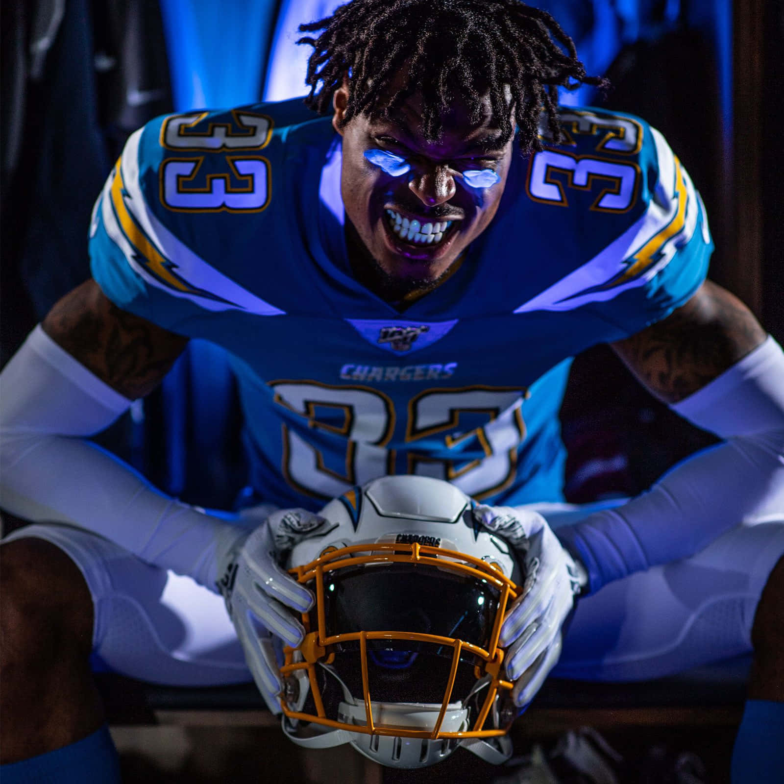NFL 桌布 壁紙 — 一名身穿藍色電光隊球衣的足球運動員在昏暗的更衣室裡拿著頭盔，激烈地咆哮。