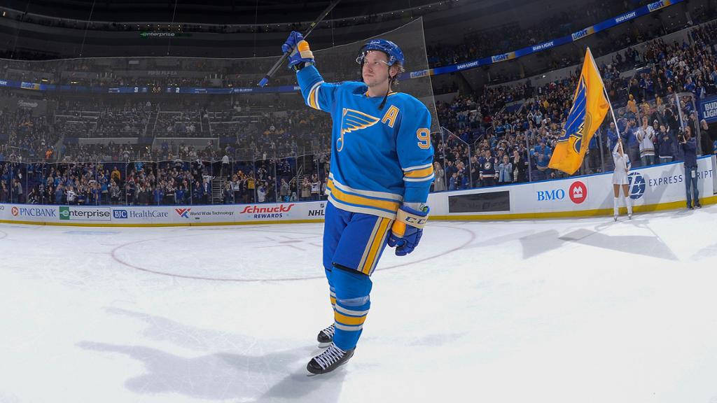 St Louis Blues 桌布 壁紙 — 一名身穿藍金球衣的聖路易斯藍調冰球球員在冰上高舉球棍慶祝勝利，場內球迷歡呼。