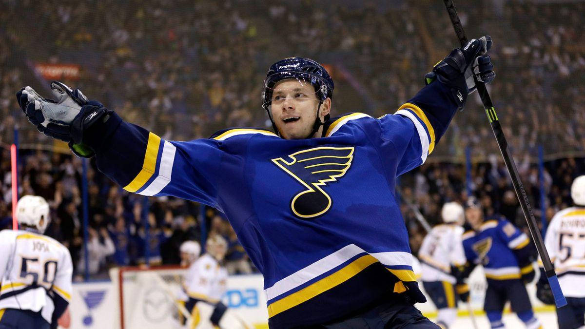 St Louis Blues 桌布 壁紙 — 一名身穿藍黃球衣的冰球運動員在明亮的場館燈光下進行激烈比賽時高舉雙臂慶祝。