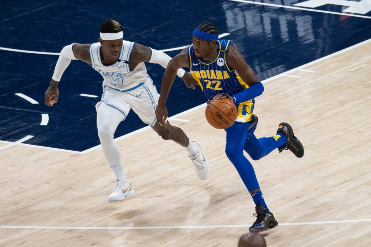 caris levert 桌布 壁紙 — 一名身穿藍黃球衣的籃球運動員在光亮的球場上，在明亮的場館燈光下，運球越過一名身穿白色球衣的防守球員。