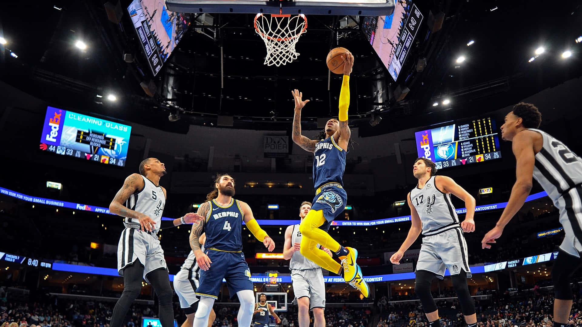 Ja Morant 動圖 桌布 壁紙 — 一名身穿藍黃球衣的籃球運動員在場館燈光下跳向籃框，防守球員在旁觀看。