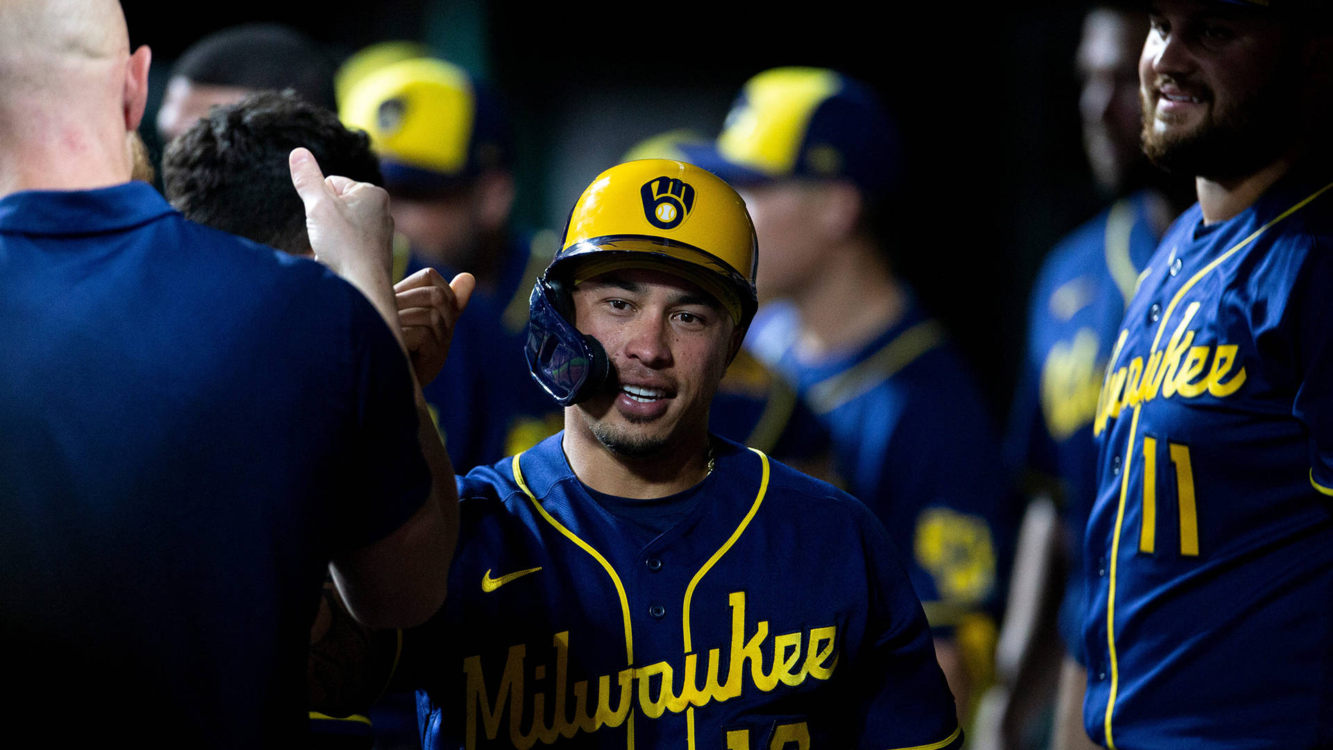 Brewers 桌布 壁紙 — 一名身穿藍黃色球衣的密爾瓦基釀酒人棒球選手在球員休息區與隊友擊掌。