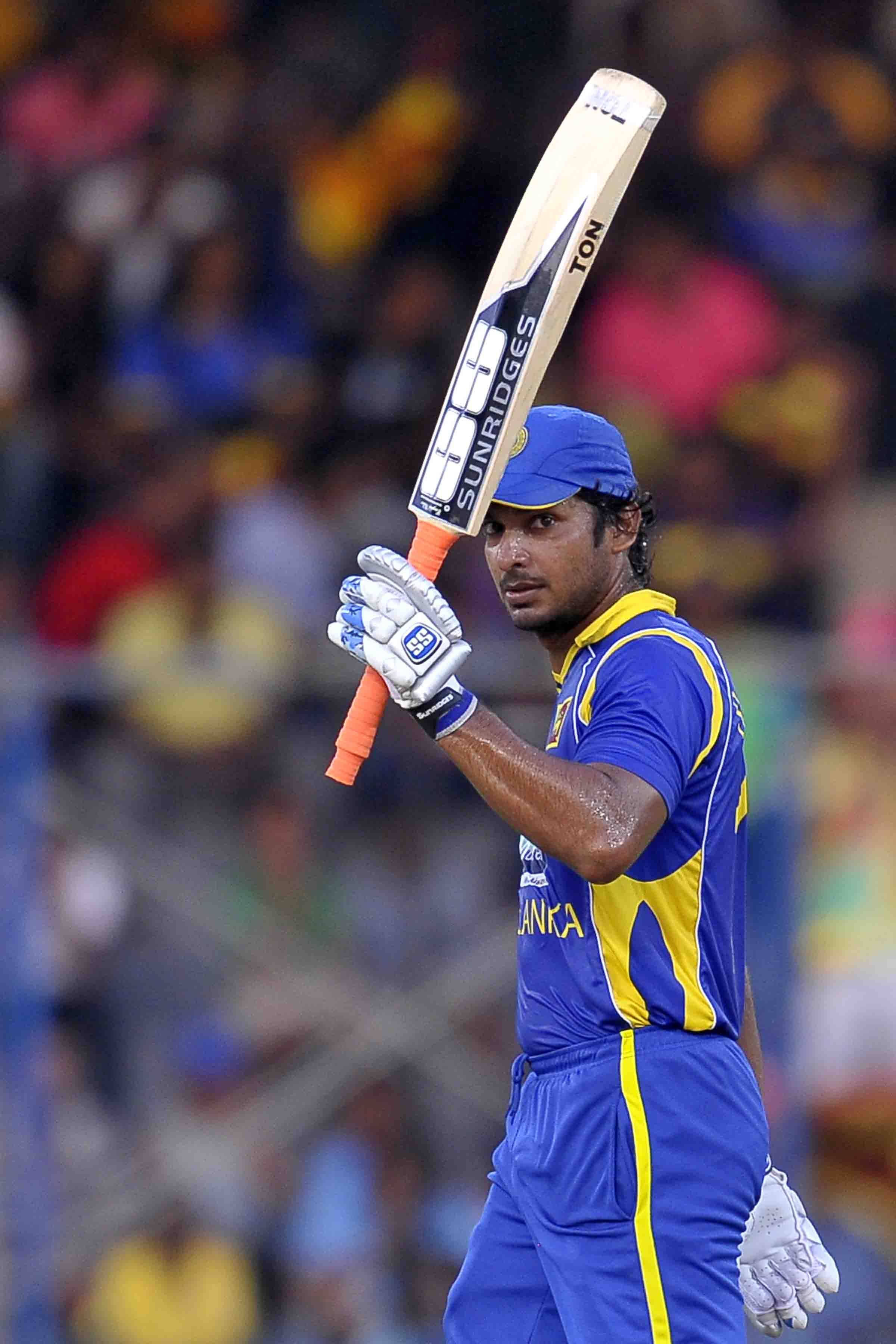 Sri Lanka Cricket 桌布 壁紙 — 一名身穿藍黃色球衣的斯里蘭卡板球手在夜間比賽中，在球場燈光下高舉球棒慶祝勝利。