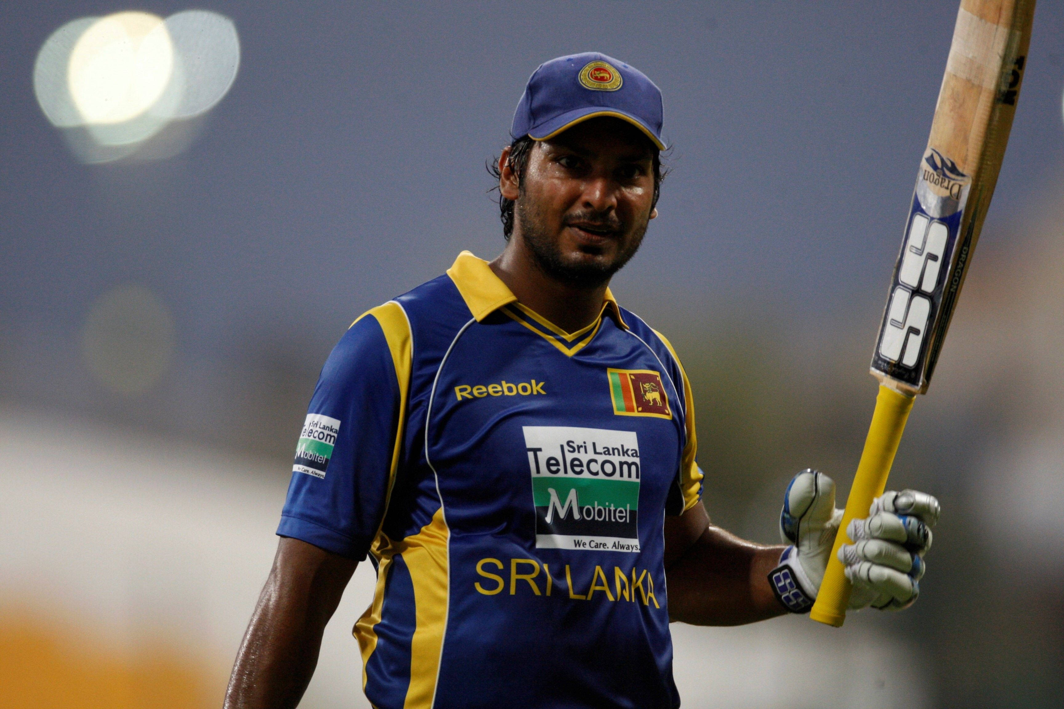Sri Lanka Cricket 桌布 壁紙 — 一名身穿藍黃色球衣的斯里蘭卡板球運動員在夜間球場燈光下手持球棒。