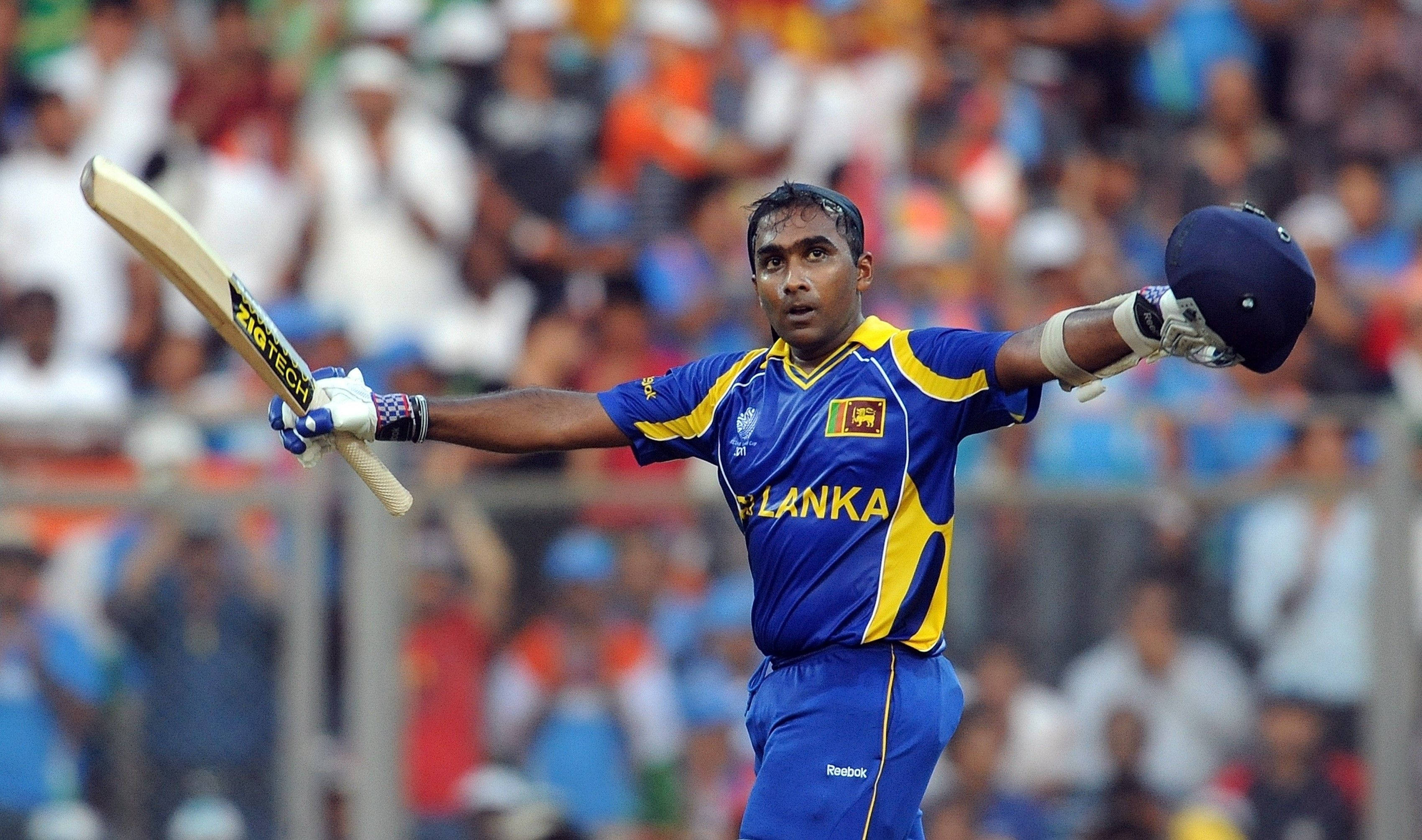 Sri Lanka Cricket 桌布 壁紙 — 一名身穿藍黃色球衣的斯里蘭卡板球運動員在歡呼的人群中高舉球棒和頭盔慶祝。