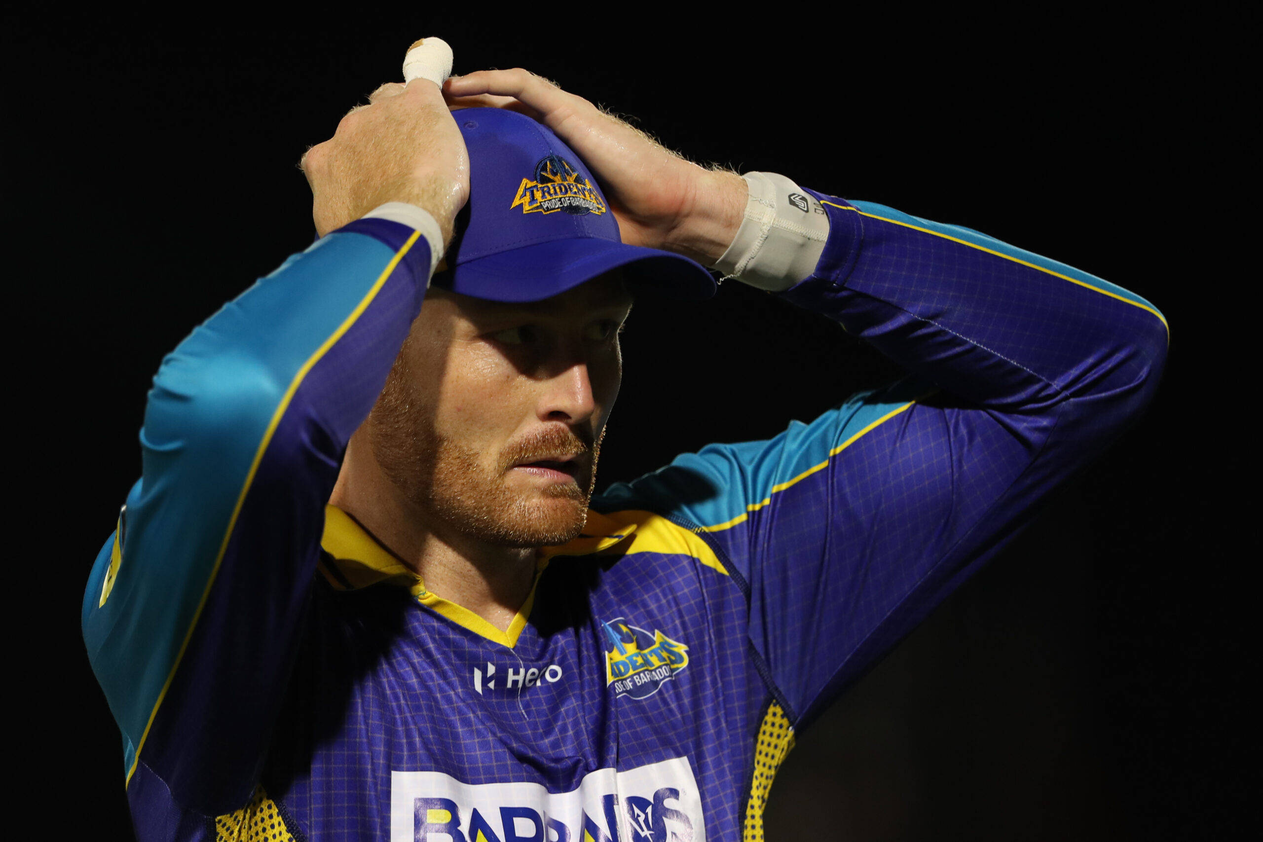 martin guptill 桌布 壁紙 — 一名身穿藍黃色球衣的板球運動員在黑色背景下沮喪地拿著帽子。
