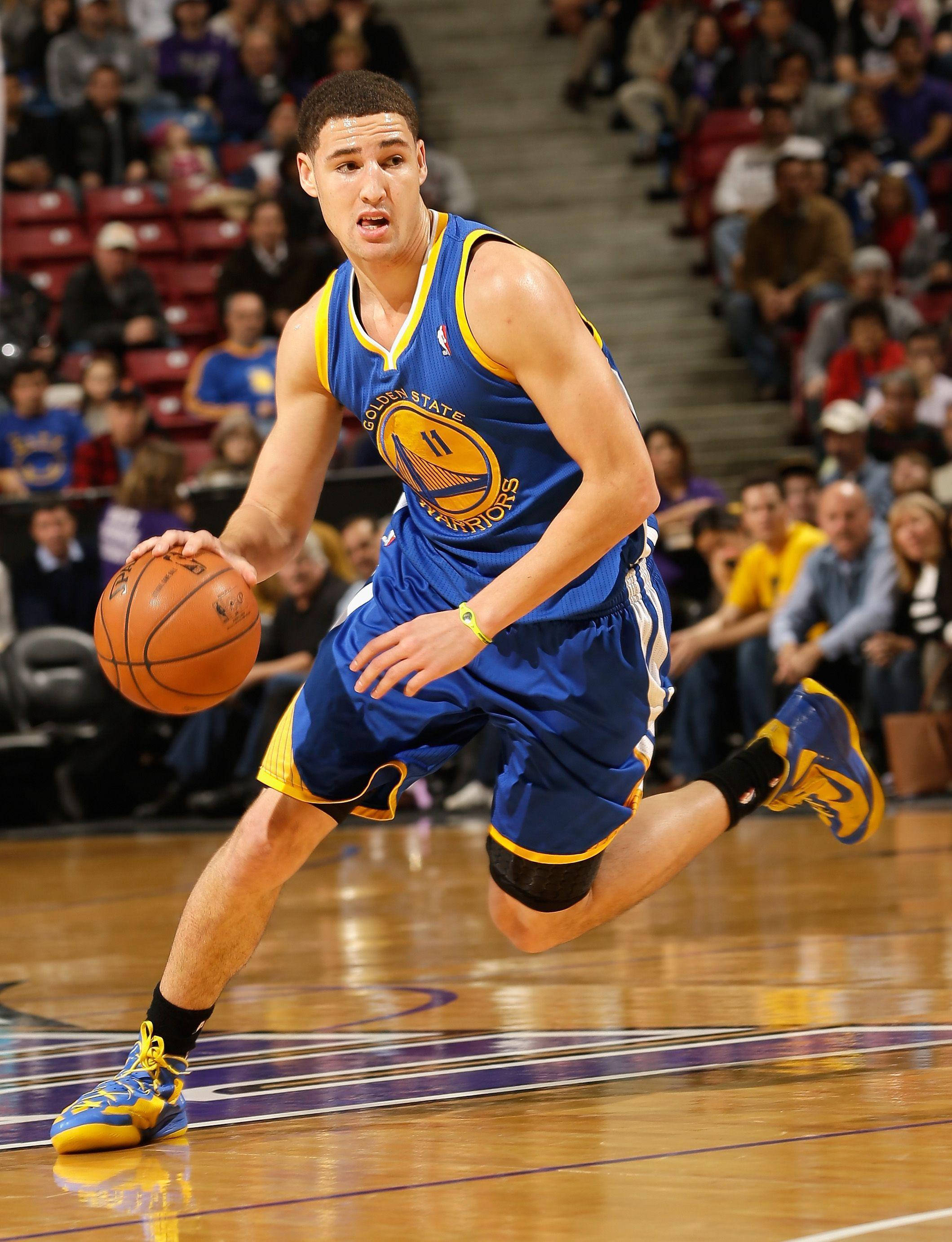 Thompson 桌布 壁紙 — 一名身穿藍黃色球衣的籃球運動員在明亮的場館燈光下，於比賽中專注地運球。