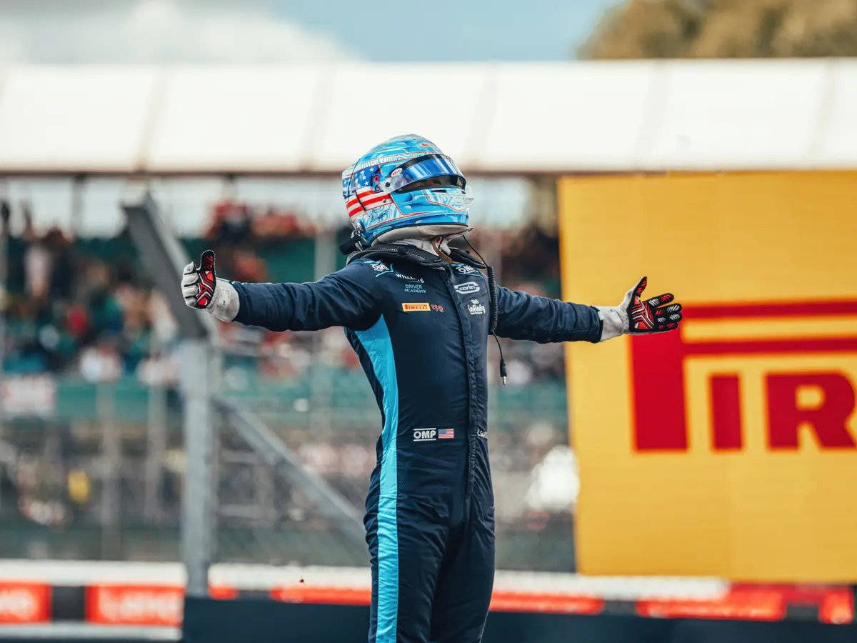 F1 桌布 壁紙 — 一名身穿藍黑色賽車服、戴著美國國旗頭盔的賽車手在賽道上張開雙臂慶祝勝利。